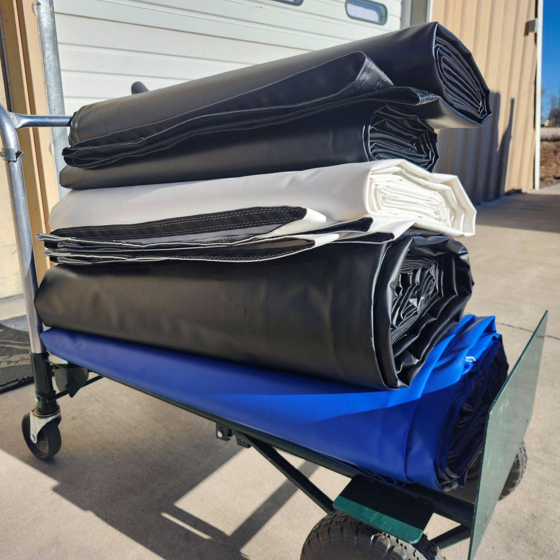 A cart loaded with several stacked, rolled-up heavy-duty vinyl tarps in black, white, and blue.