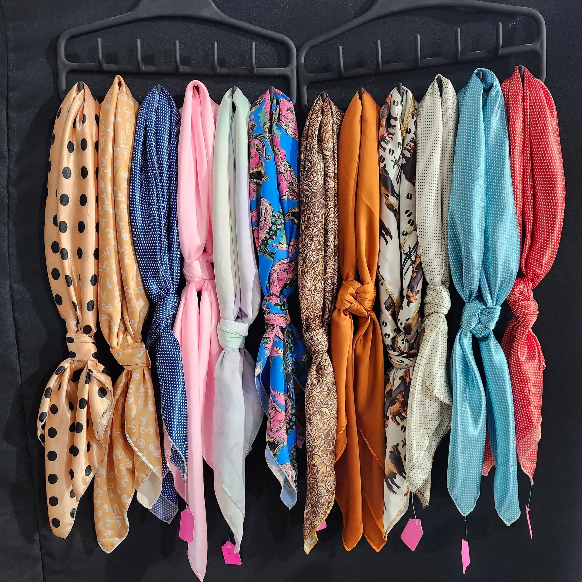 A variety of scarves in different colors and patterns are hung in a row on two dark plastic hangers.