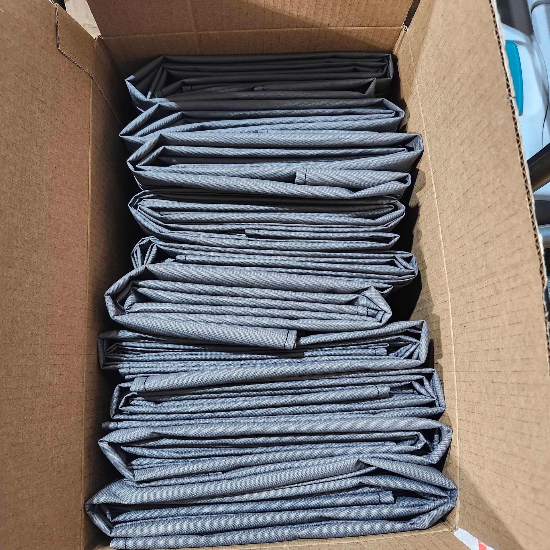 A box filled with neatly stacked, folded gray fabric material.