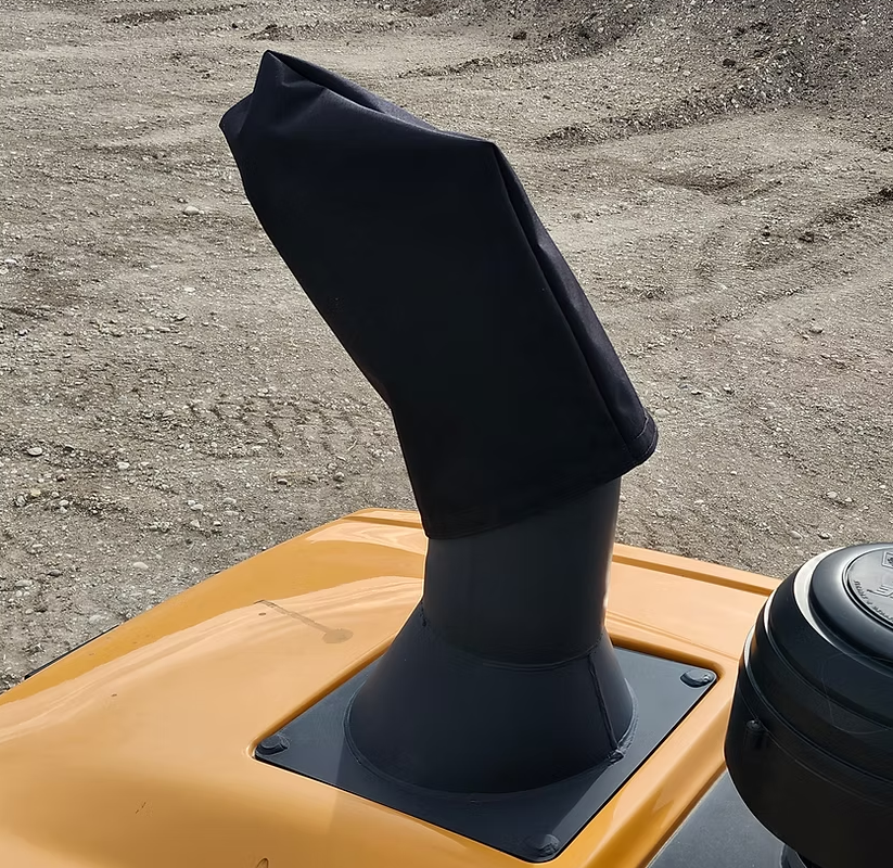A black fabric exhaust cover on a yellow tractor, set against a gravel background.