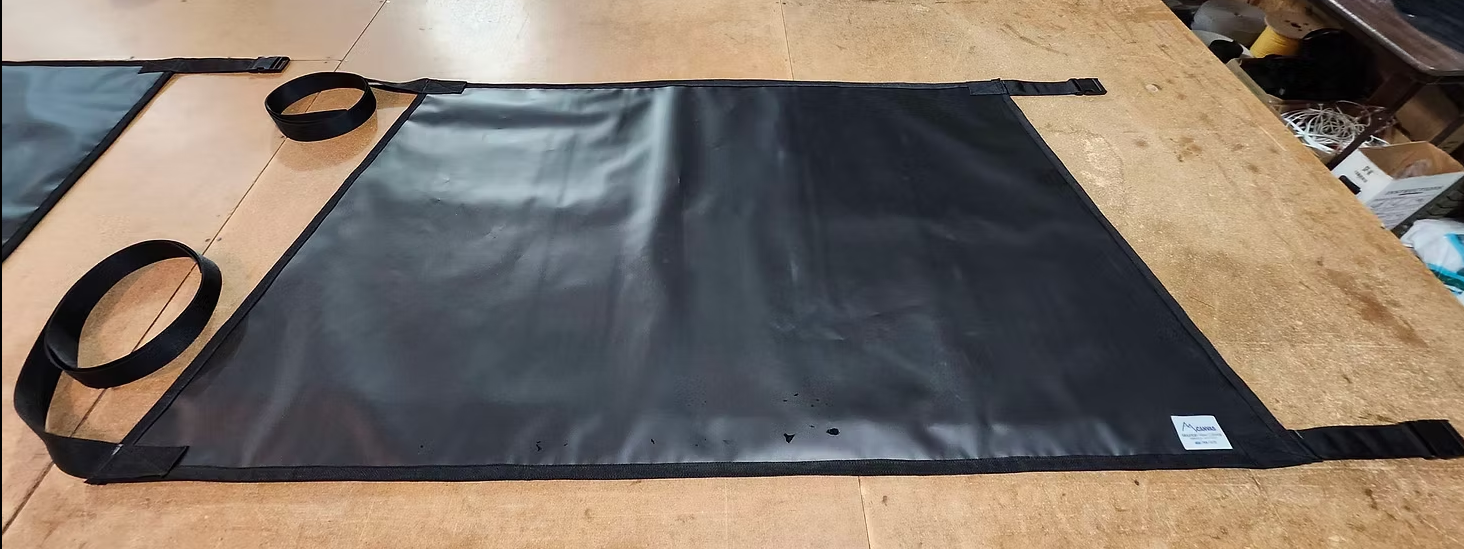 A rectangular black vinyl transfer sling with four fabric loops, laid flat on a wooden work surface.