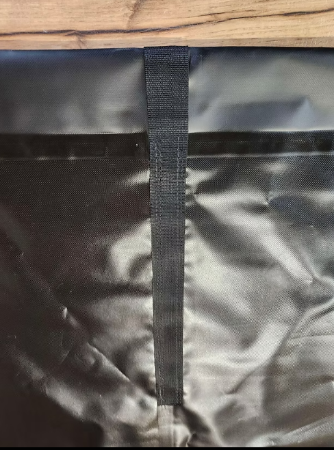 A black, textured fabric material featuring a vertical, reinforced stitched webbing strap centered on the surface.