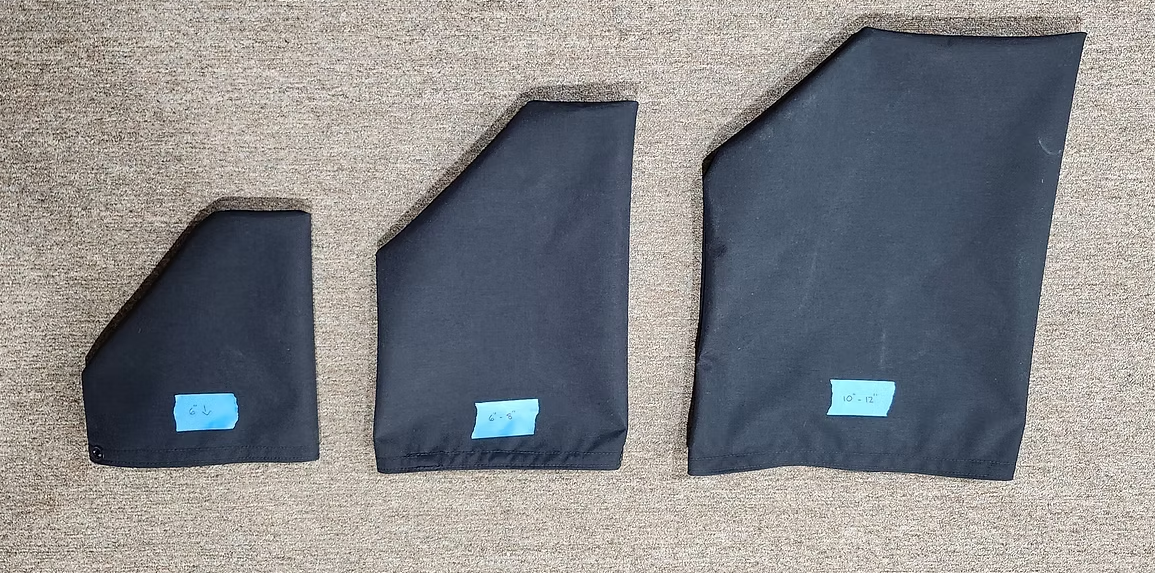 Three black, irregularly shaped fabric pieces of varying sizes, each with a small blue adhesive label, on a carpeted floor.