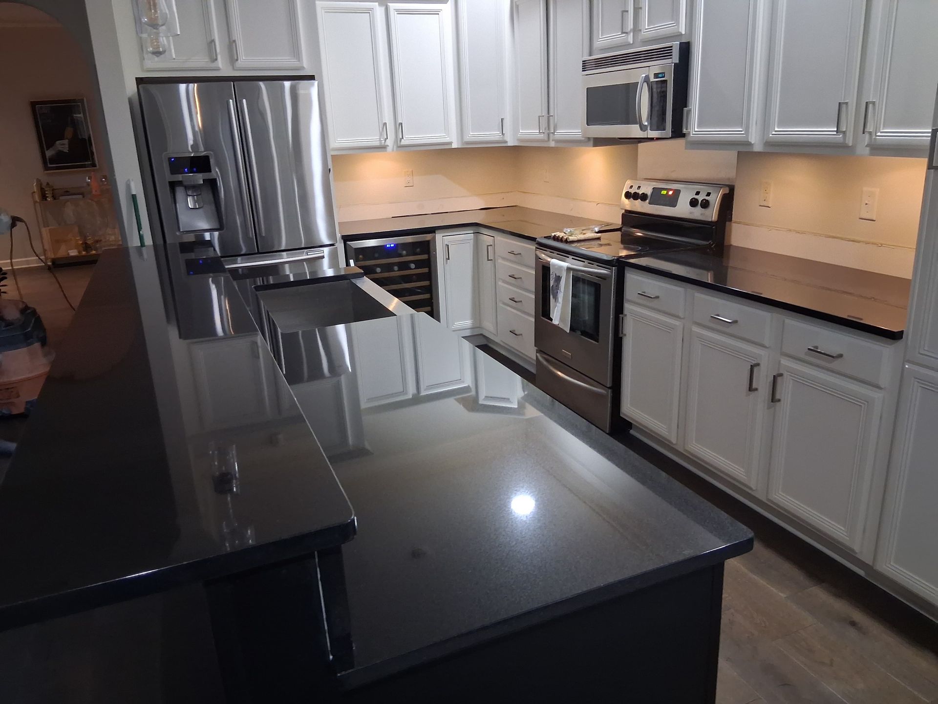 Modern kitchen with black island, stainless steel appliances, white cabinets, and tiled backsplash