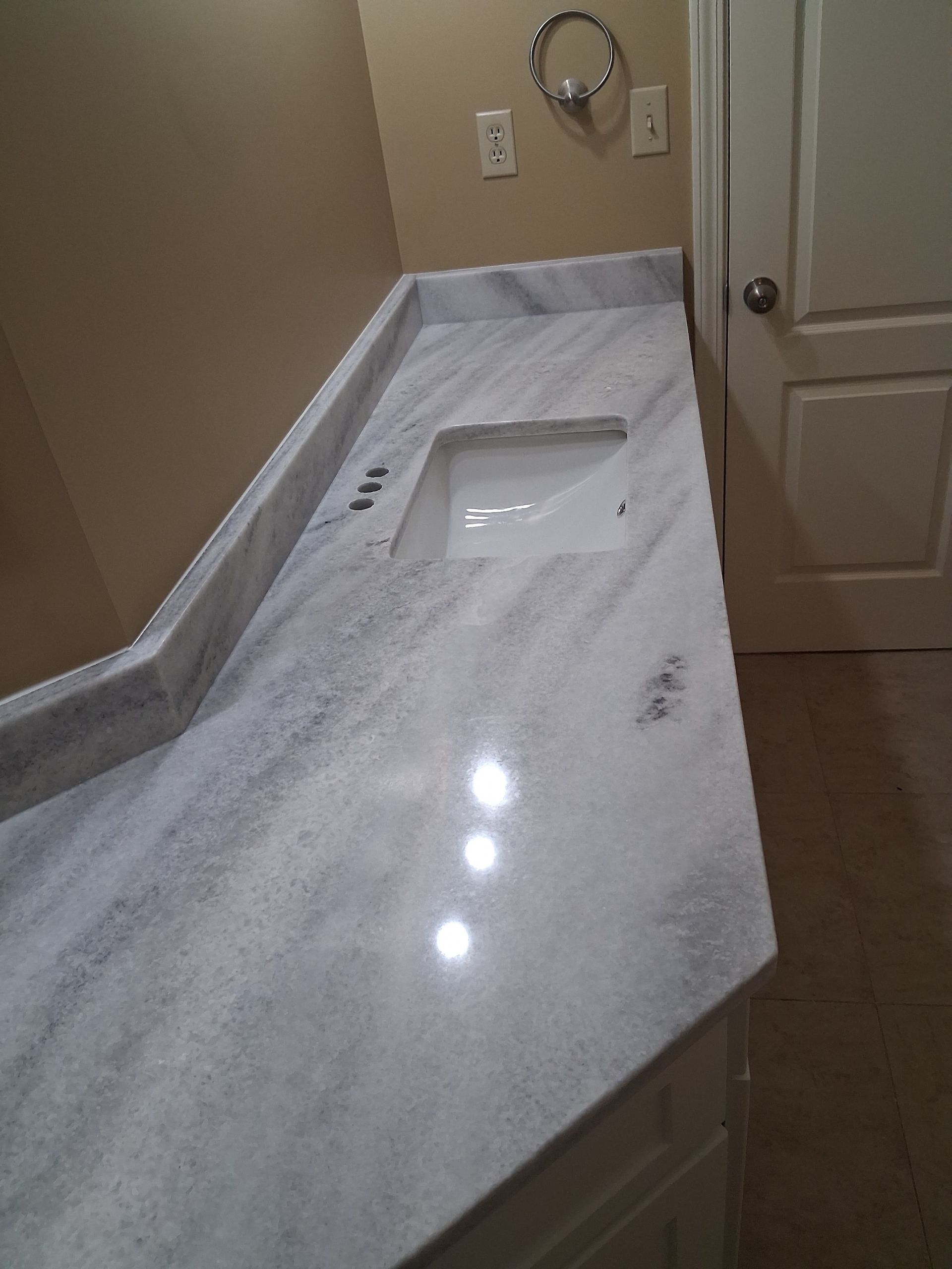 Bathroom vanity with white marble countertop and sink, beige walls, and a towel ring.