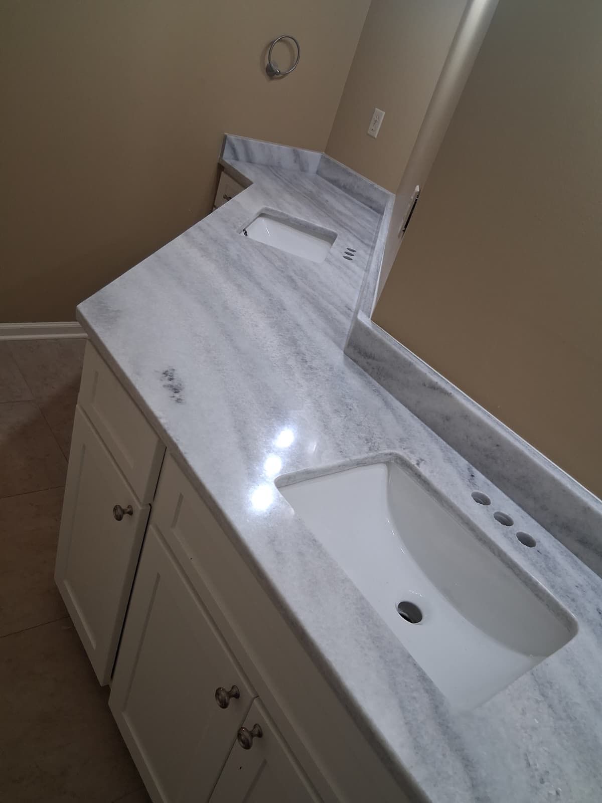 Bathroom vanity with white marble countertop, two sinks, and beige walls