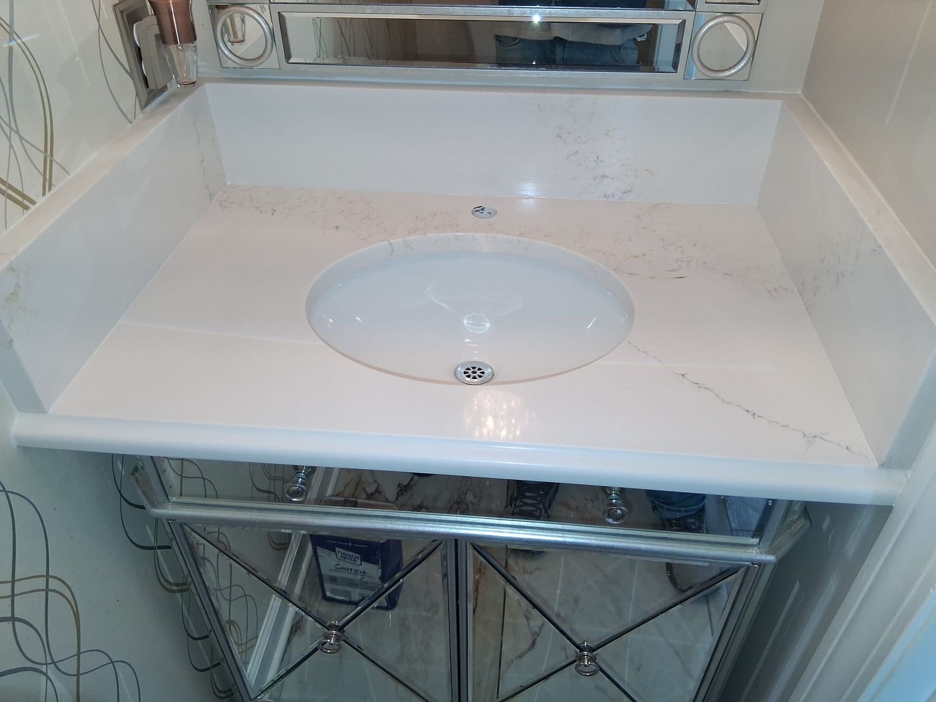 Bathroom sink vanity with white countertop, oval basin, and chrome faucet under a mirror.