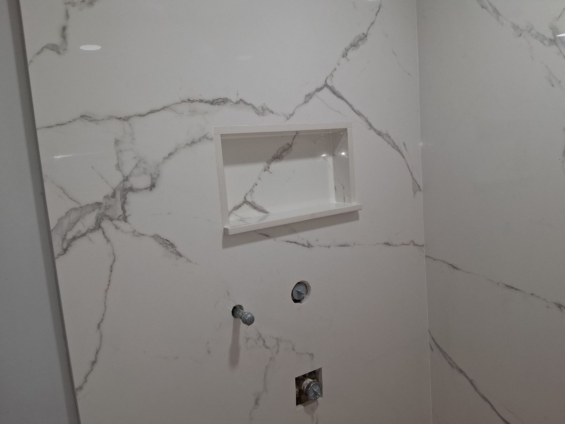 Marble-look tiled wall with built-in niche and exposed plumbing fixtures for a shower or bathroom sink