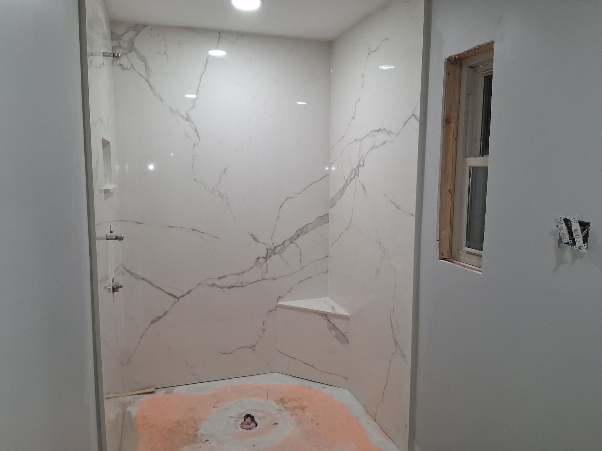 Tiled bathroom shower under renovation with a small window and exposed plumbing hole in the floor.