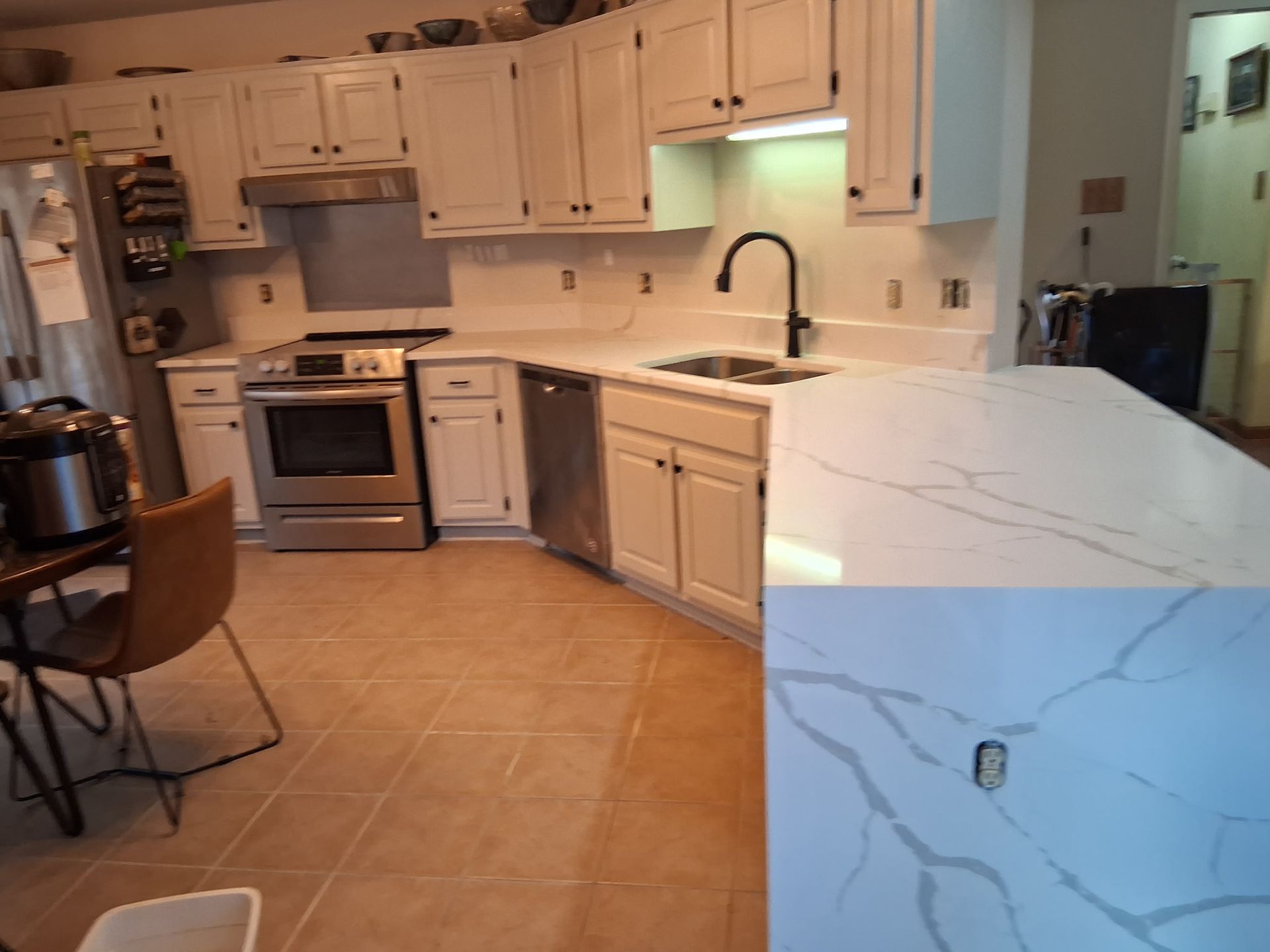 Bright kitchen with white cabinets, stainless stove, marble island, and tan tile floor.