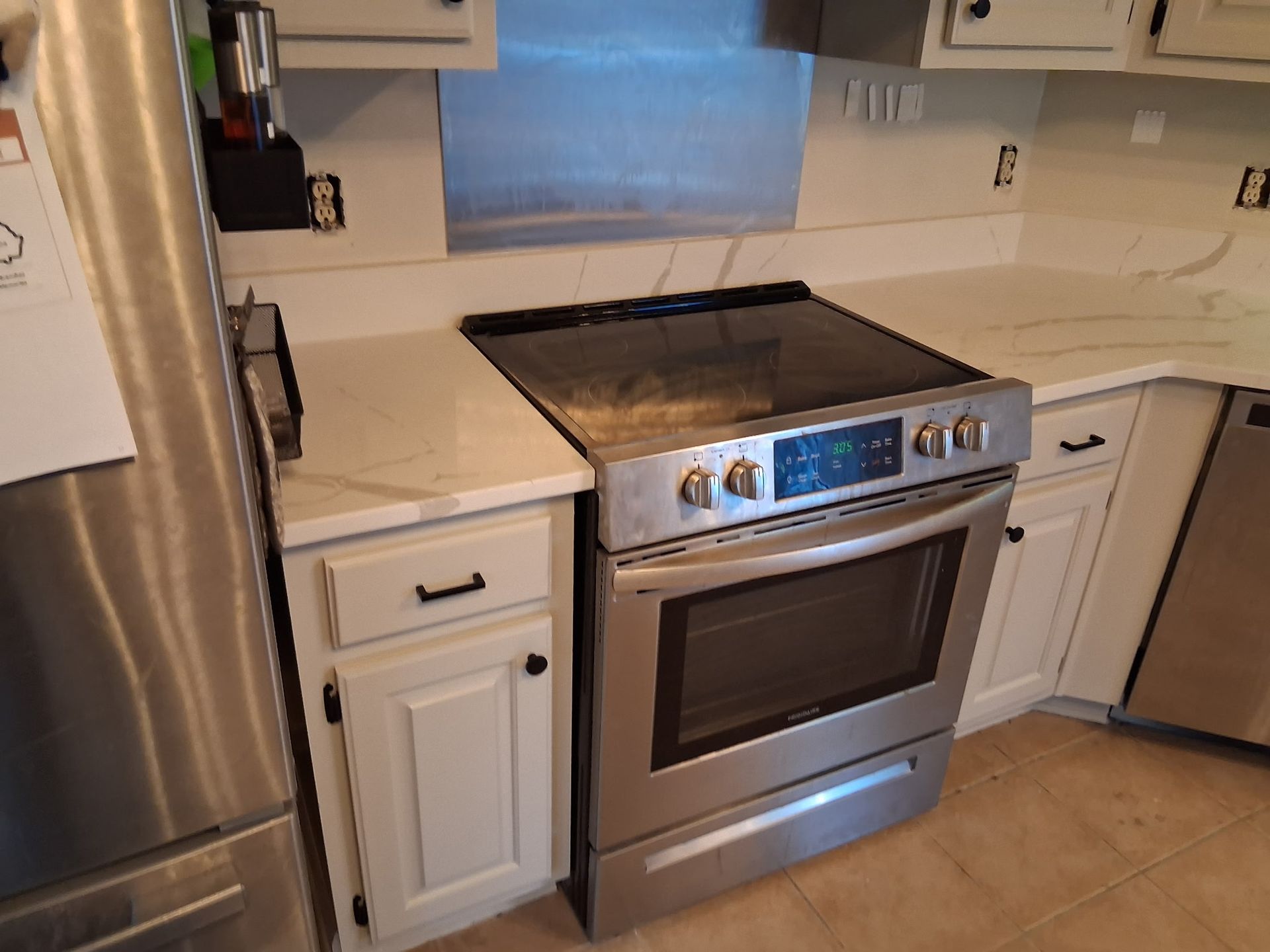 Modern kitchen with stainless steel range, white cabinets, and beige countertops, viewed at an angle