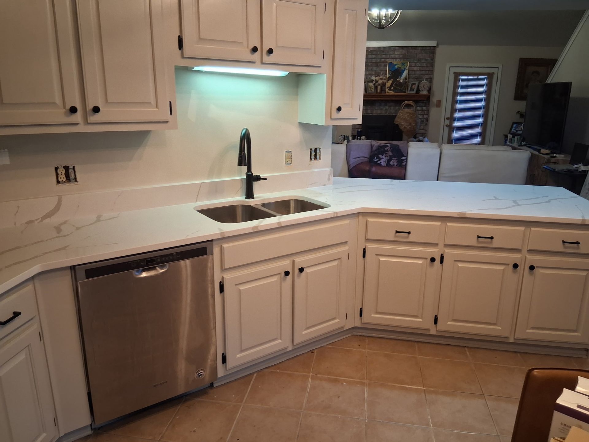 Modern kitchen with light wood cabinets, stainless dishwasher, white countertops, and a sink under under-cabinet lighting