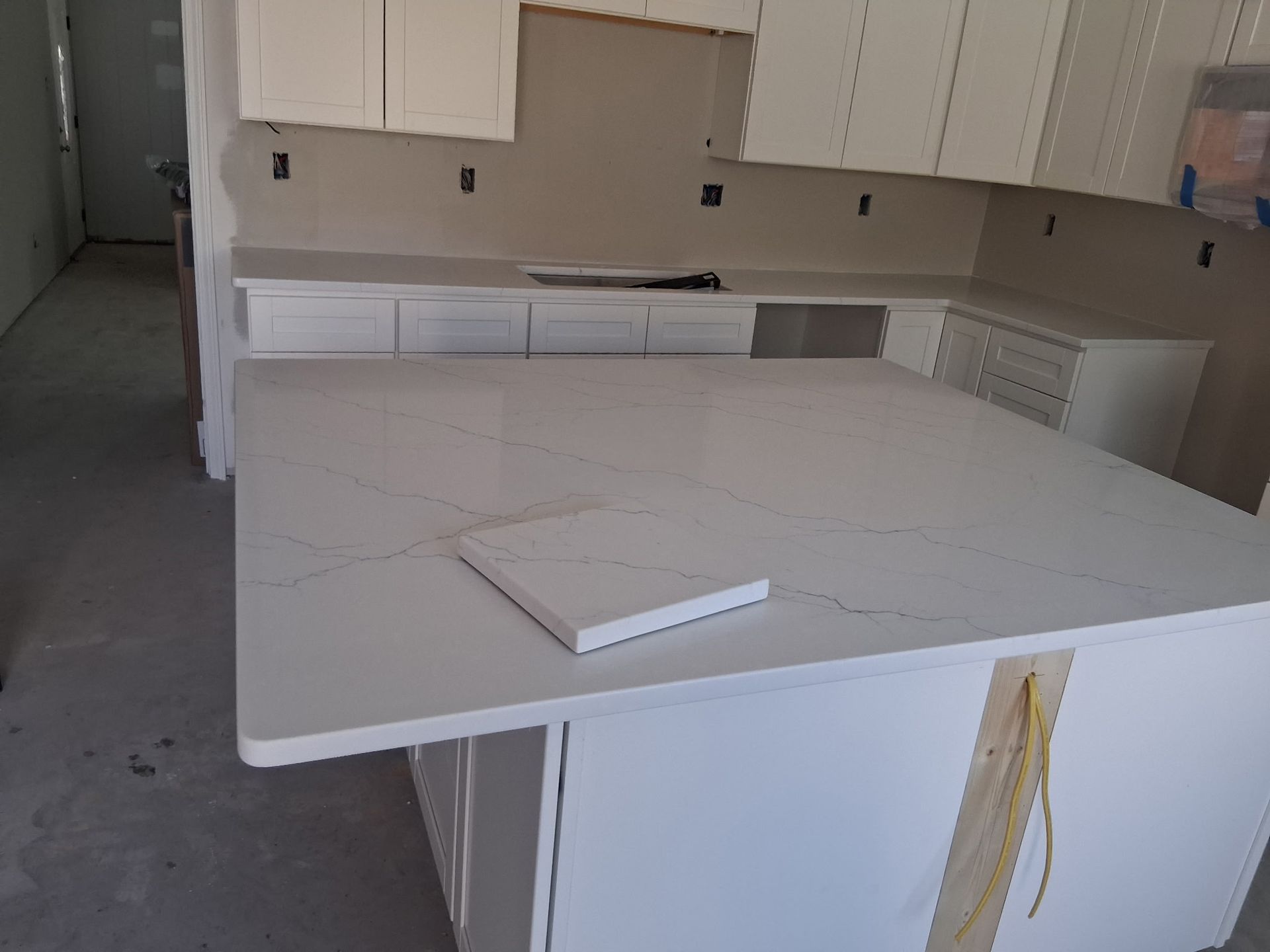 Kitchen under renovation with white cabinets and a large white island countertop, a tool resting on it.
