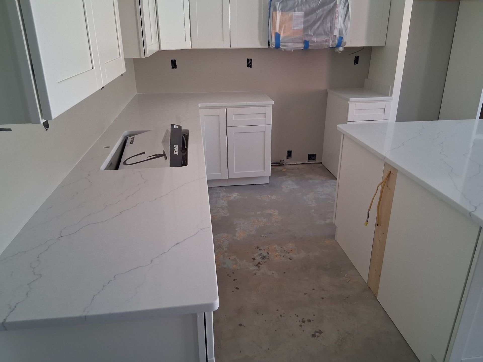 Modern kitchen under construction with white cabinets, island, and unfinished floor