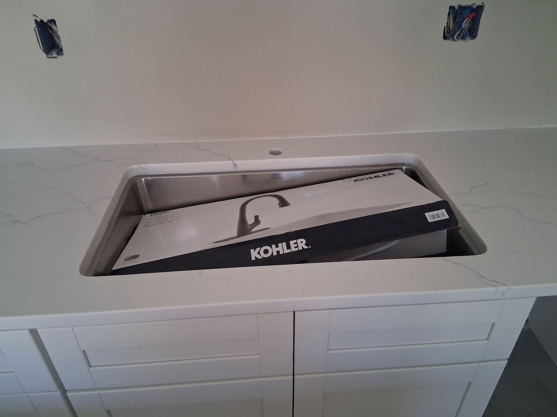 Undermount kitchen sink with a black Kohler insert set into a light gray countertop.