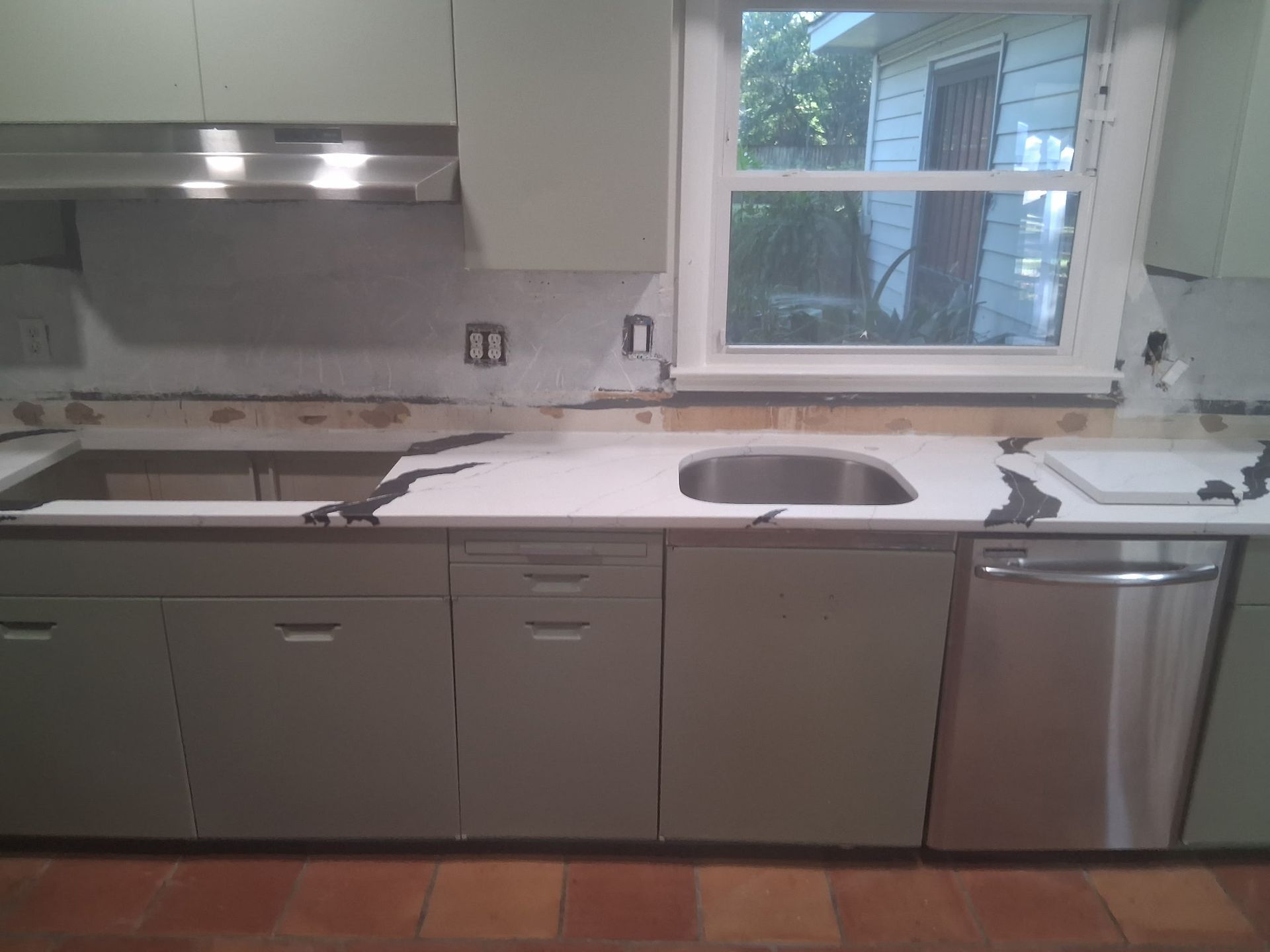 Modern kitchen with gray cabinets, white countertop, sink by a window, and stainless-steel dishwasher
