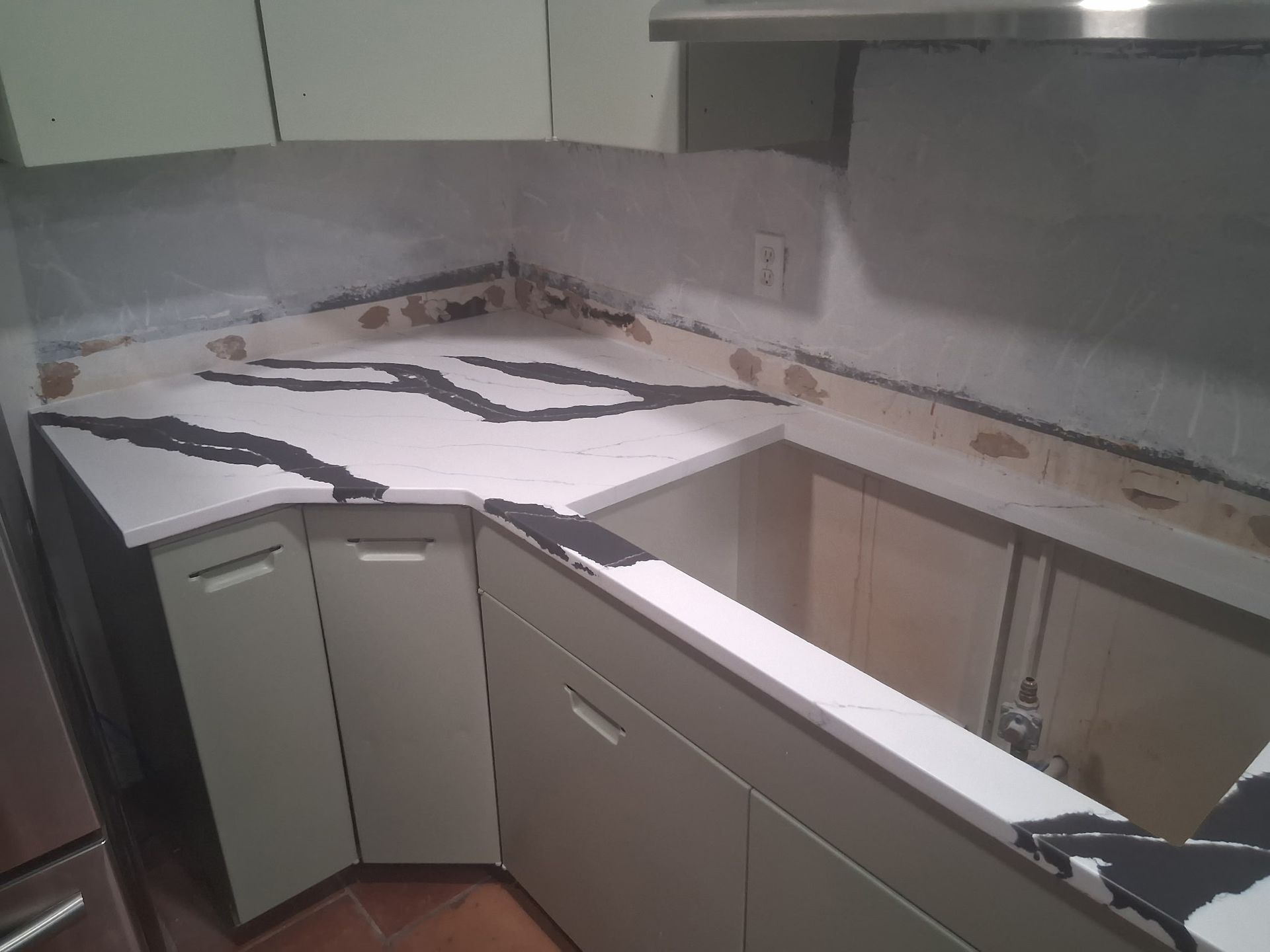 Damaged kitchen with broken countertop and cabinets, white cabinets, and debris scattered along the backsplash.