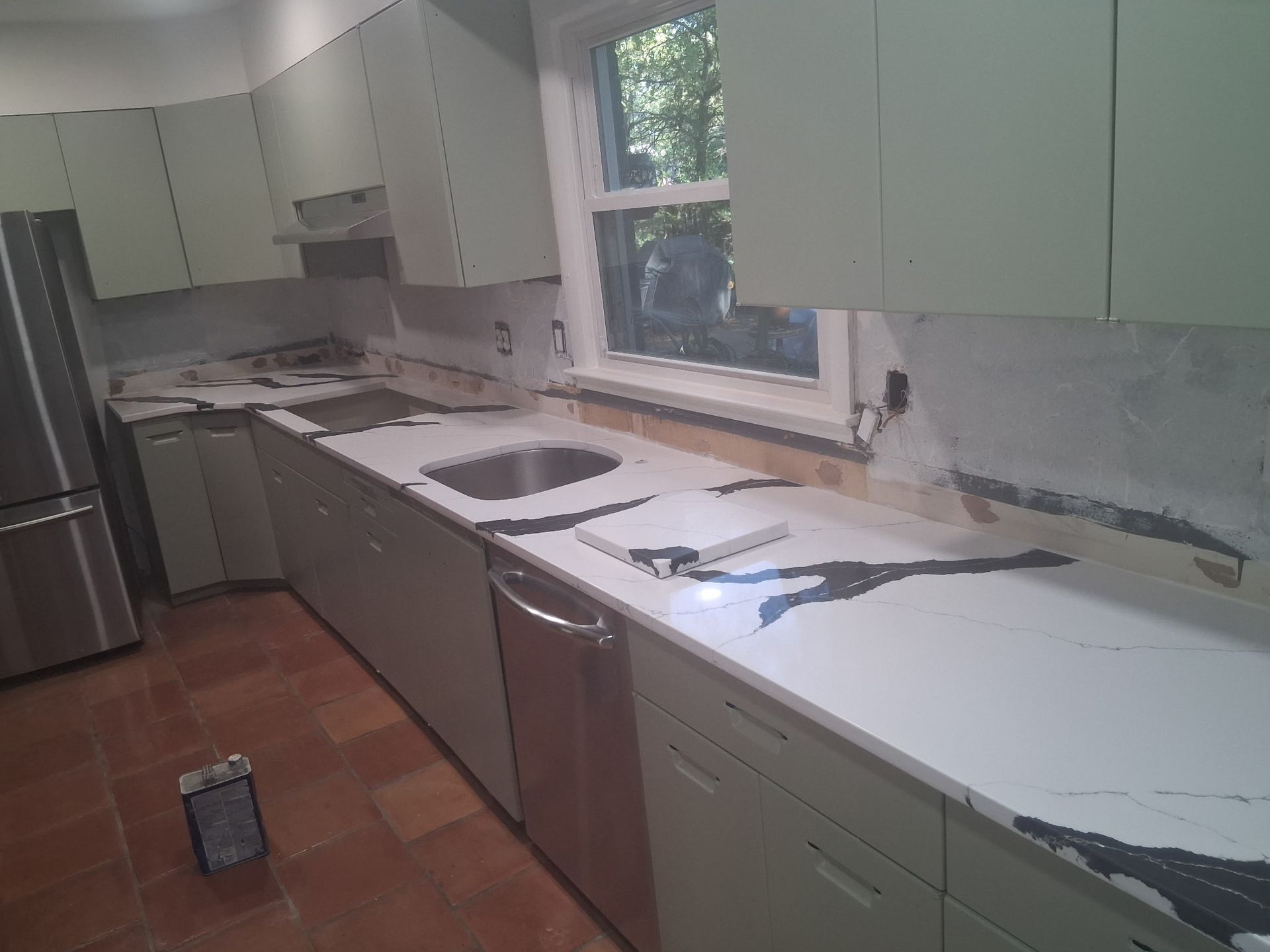 Kitchen under renovation with green cabinets, bare countertop, and exposed wall behind the sink and stove.