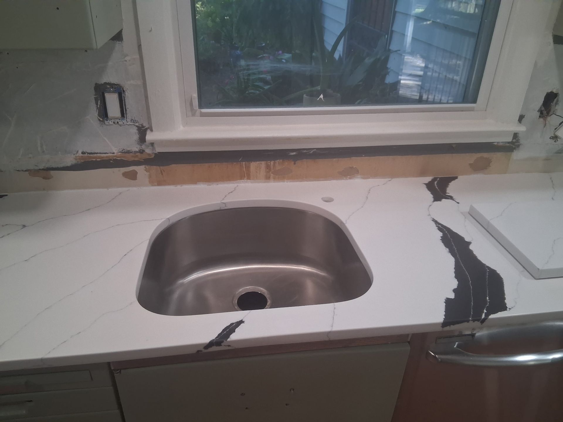 Damaged kitchen countertop with a sink cutout and torn white surface beneath a window.