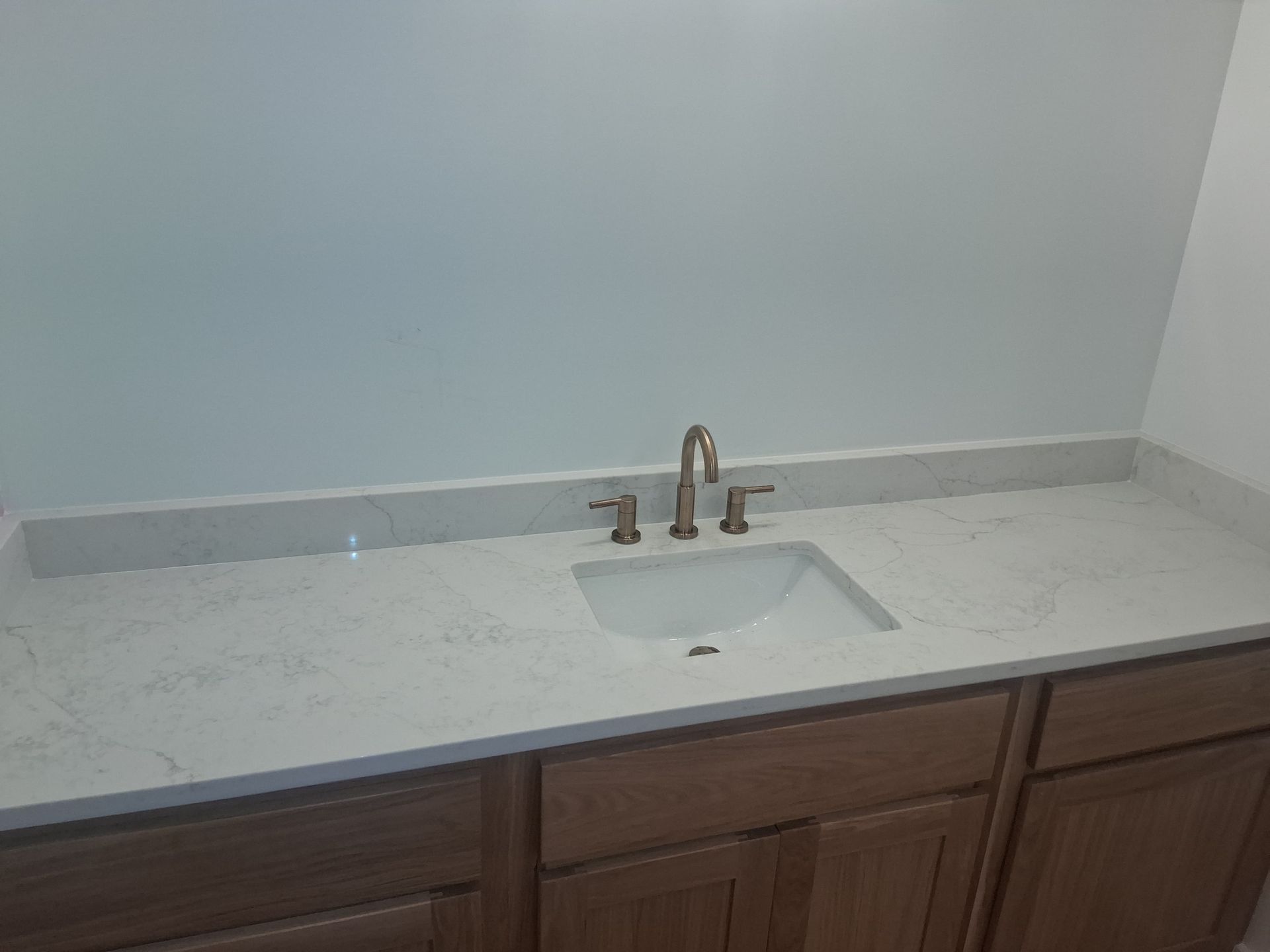 Bathroom vanity with white countertop, under-mount sink, and bronze faucet above dark wood cabinets.