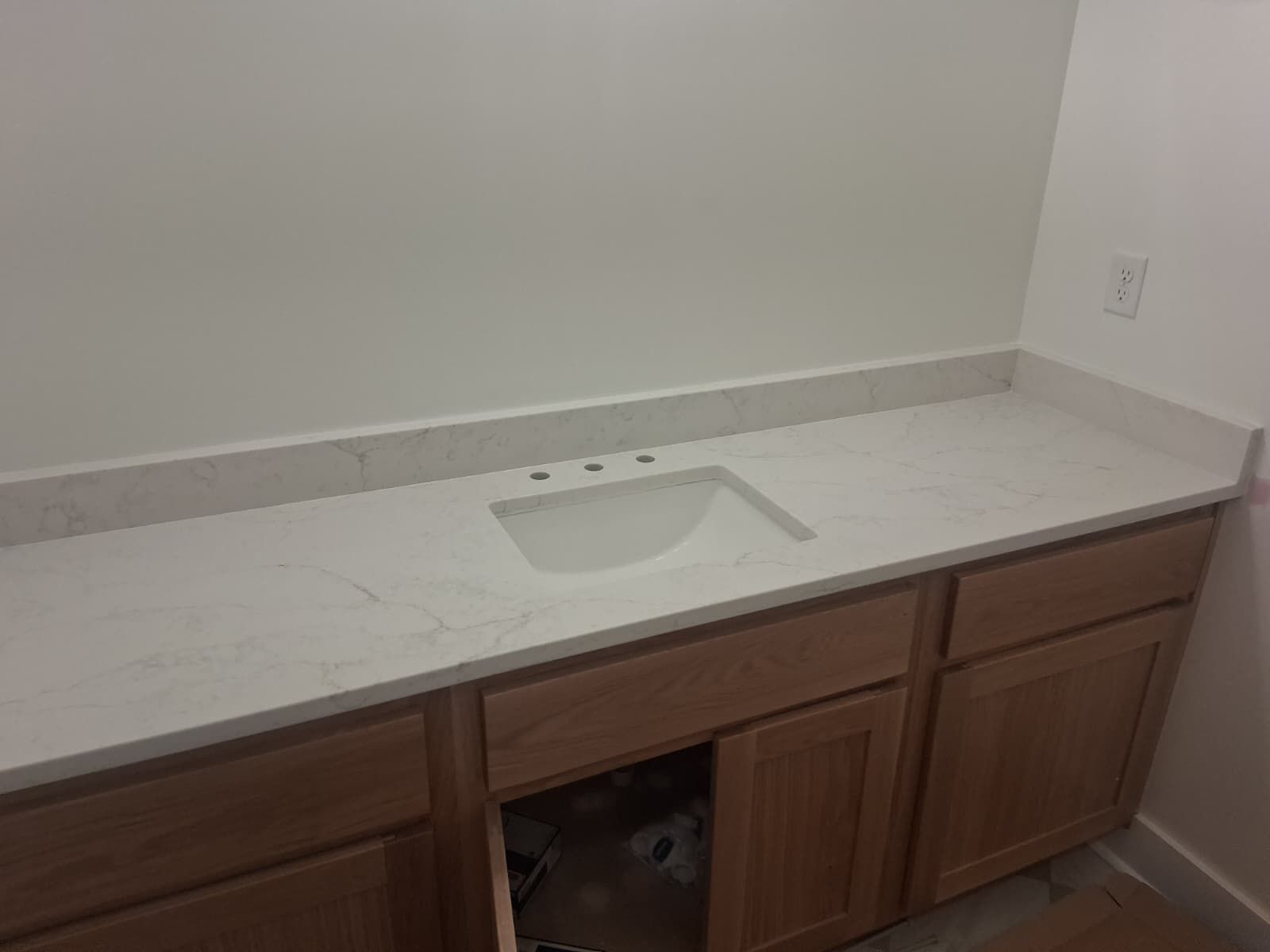 Bathroom vanity with white countertop and sink, wooden cabinets, and a pet peeking from the open center cabinet.