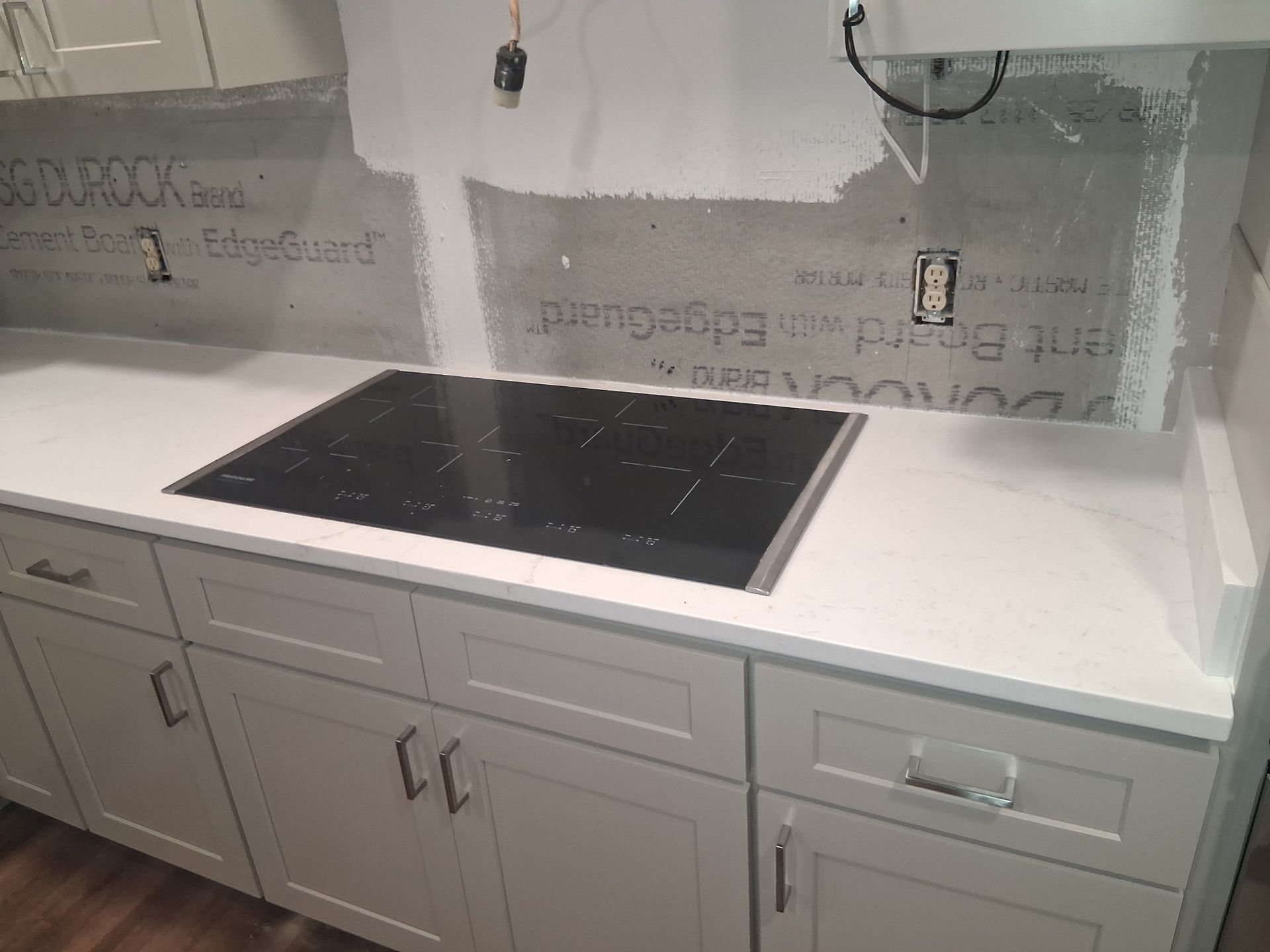 Modern kitchen countertop with a black induction cooktop, white cabinets, and unfinished backsplash area.