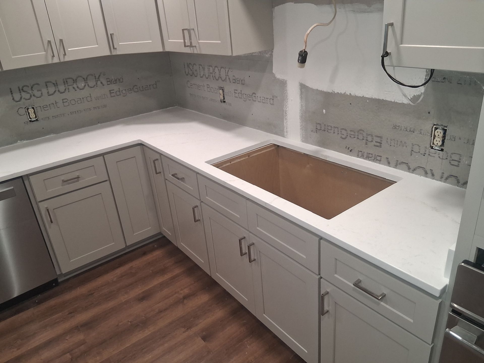 Empty U-shaped kitchen with white cabinets, gray backsplash, wood-look floor, and a cutout for a sink