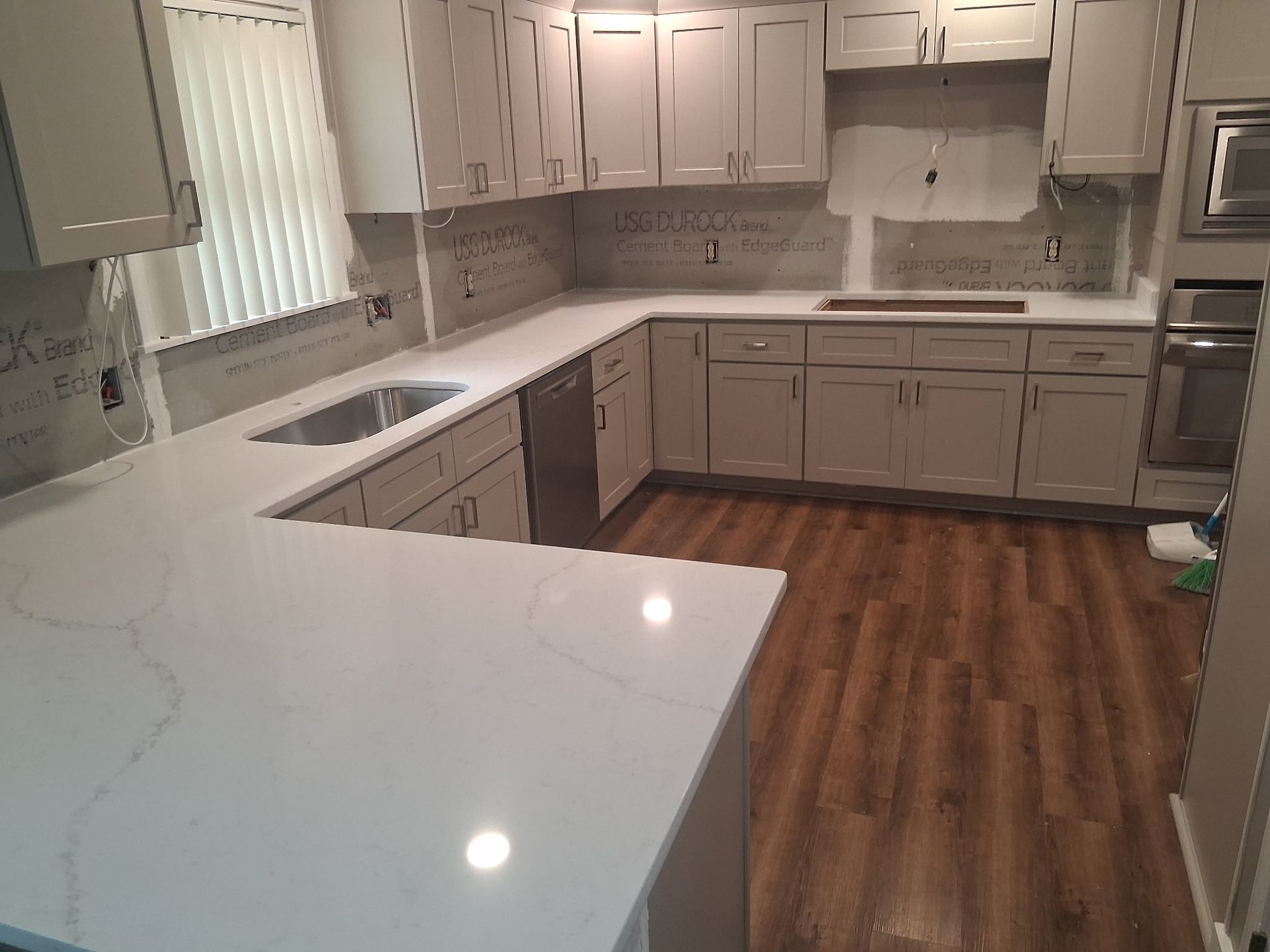 Bright white kitchen with gray cabinets, stainless appliances, and wood-look flooring