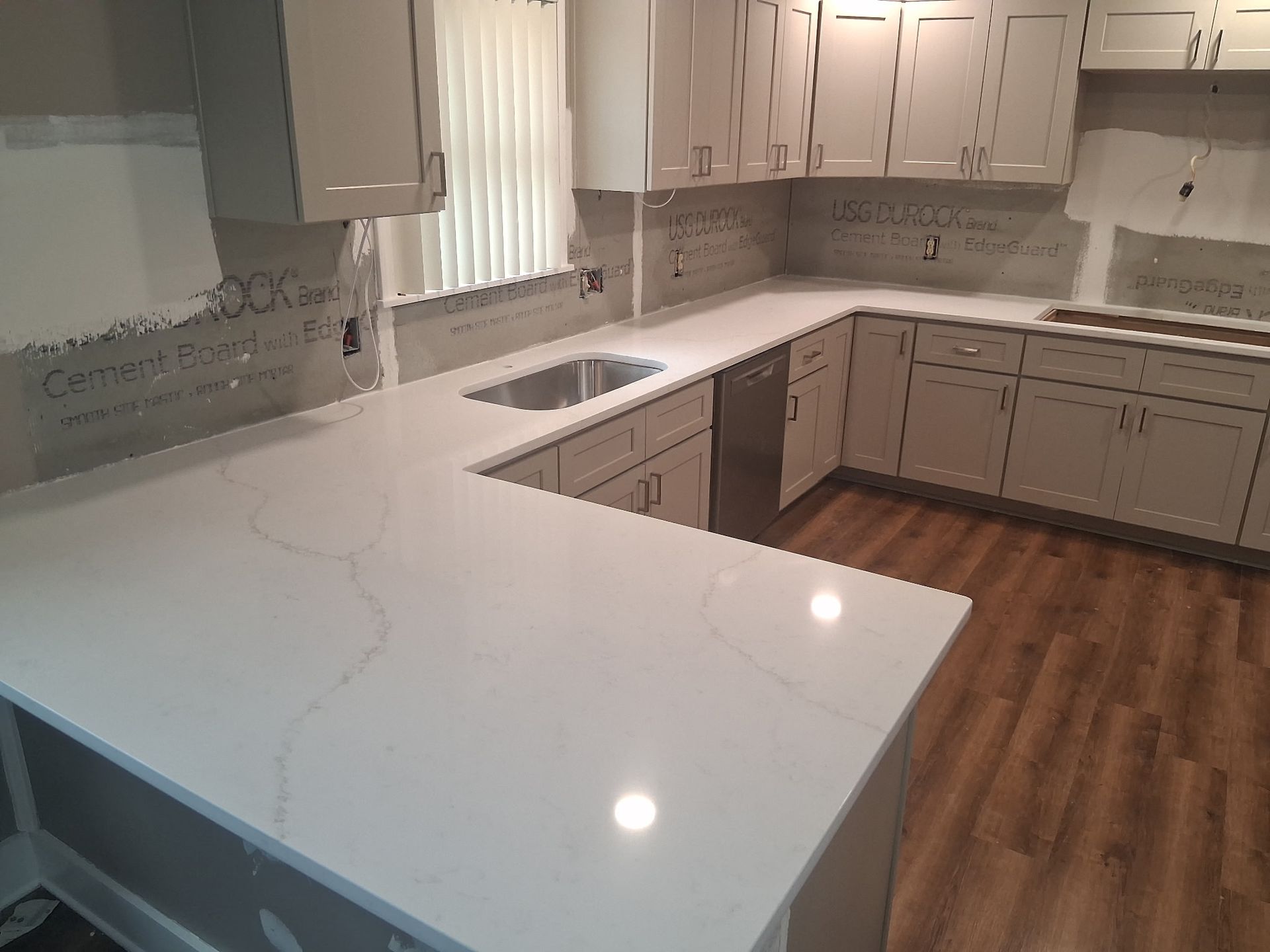 Modern kitchen with white marble island, light wood cabinets, stainless sink, and wood flooring