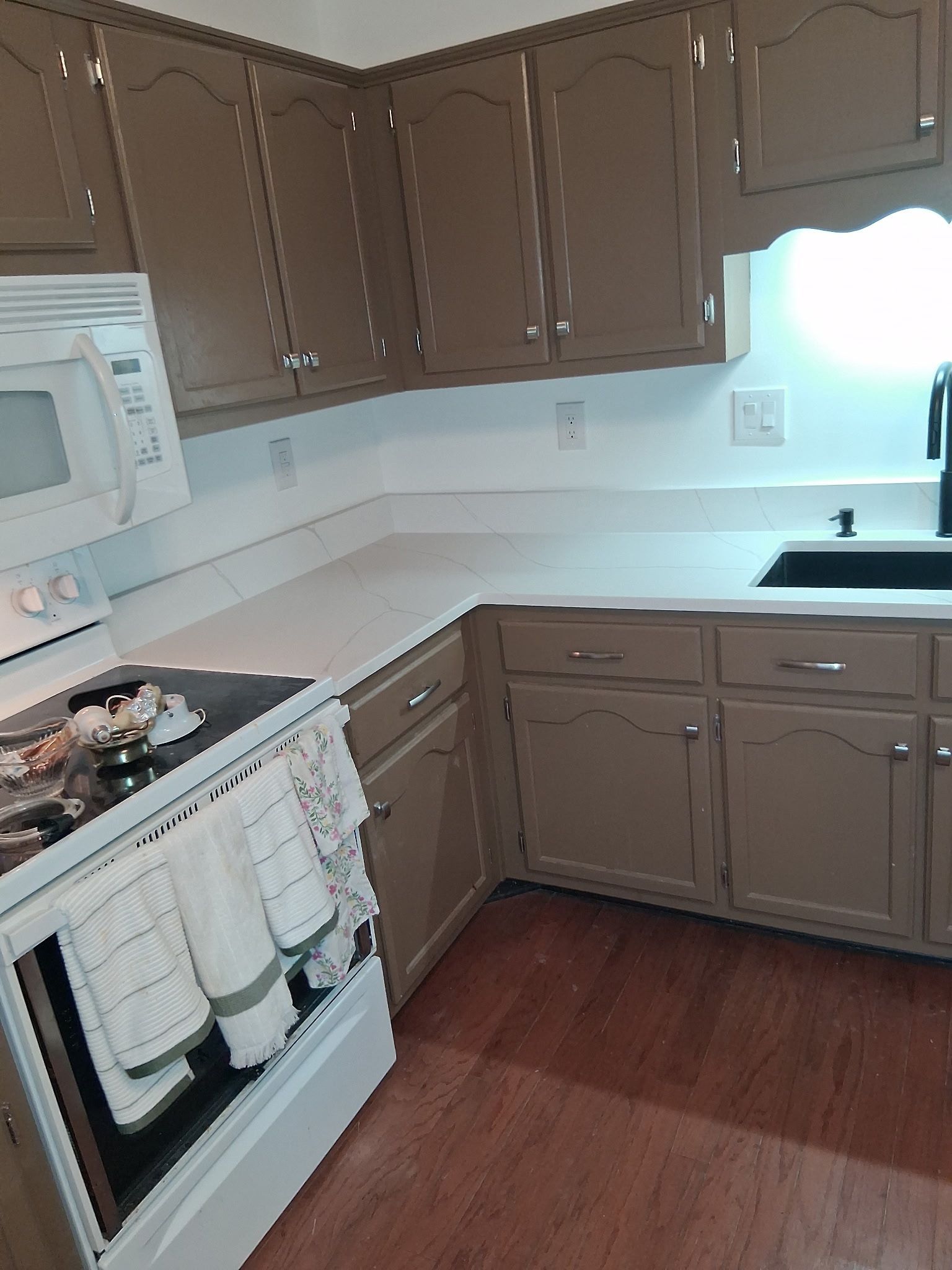 Small kitchen with brown cabinets, white appliances, countertop, and hardwood floor.