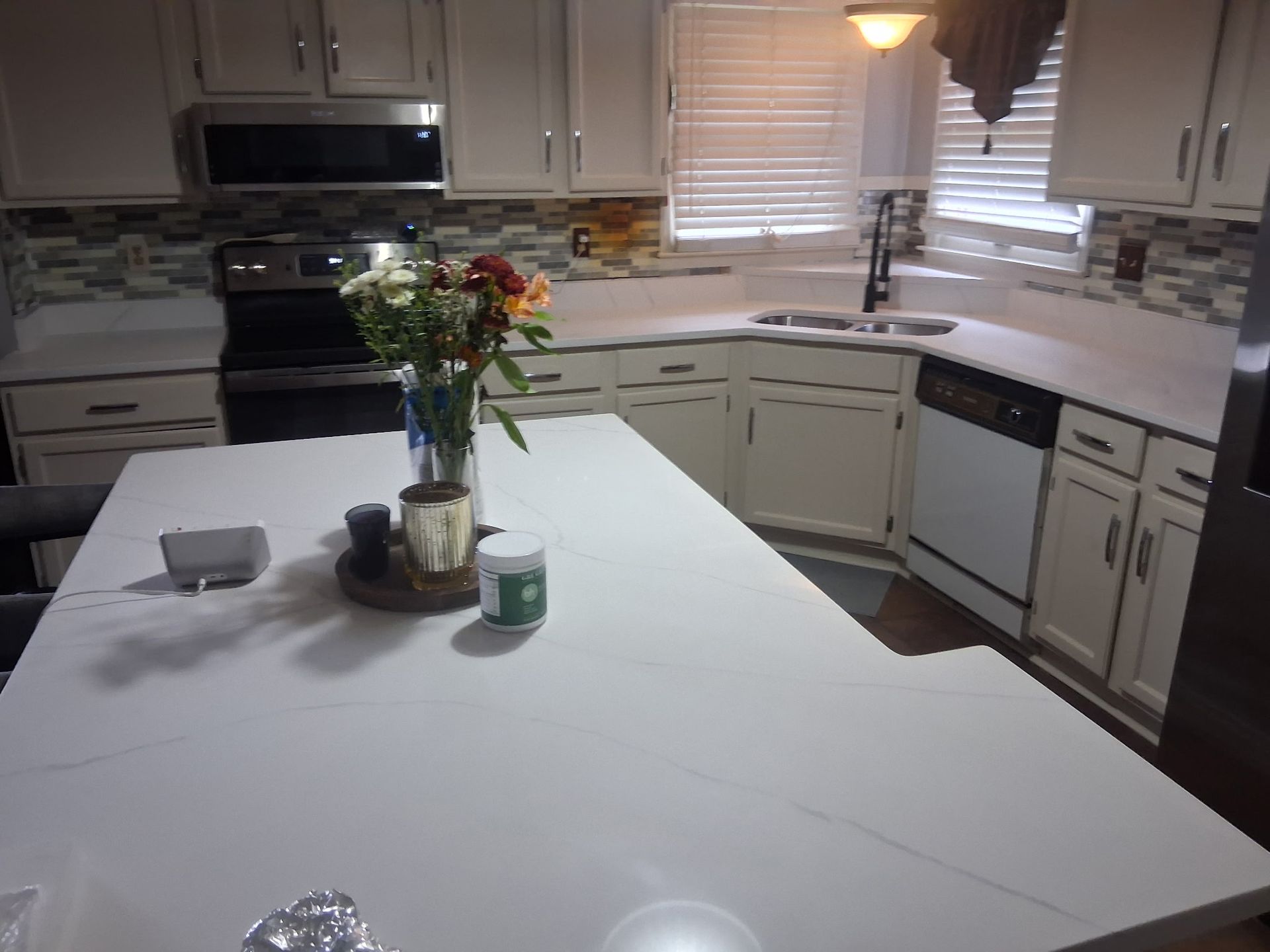 Kitchen with white island, flowers in a vase, and light cabinets near a window.