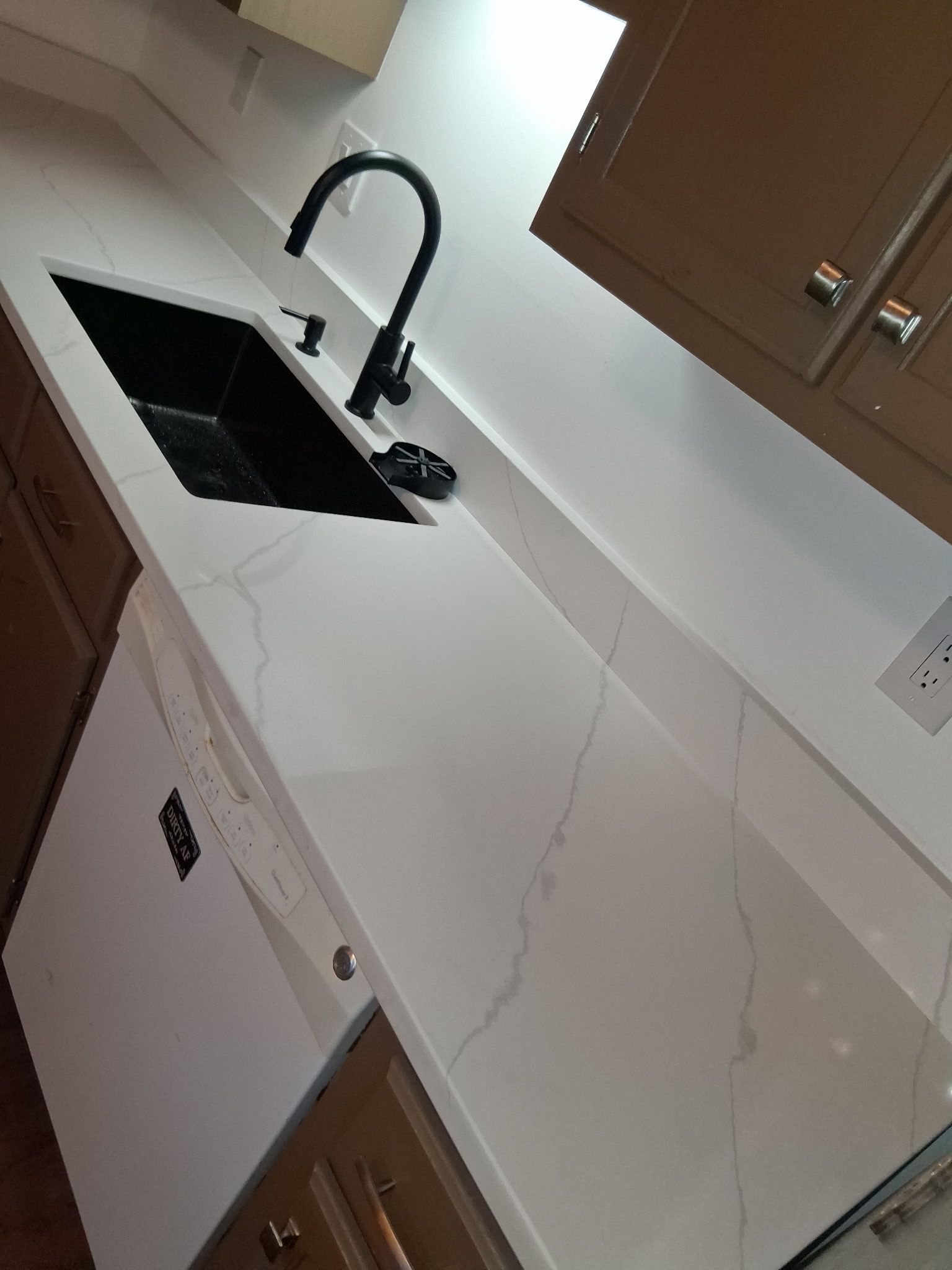 Modern kitchen with black sink and faucet, white marble countertop, and brown cabinets.