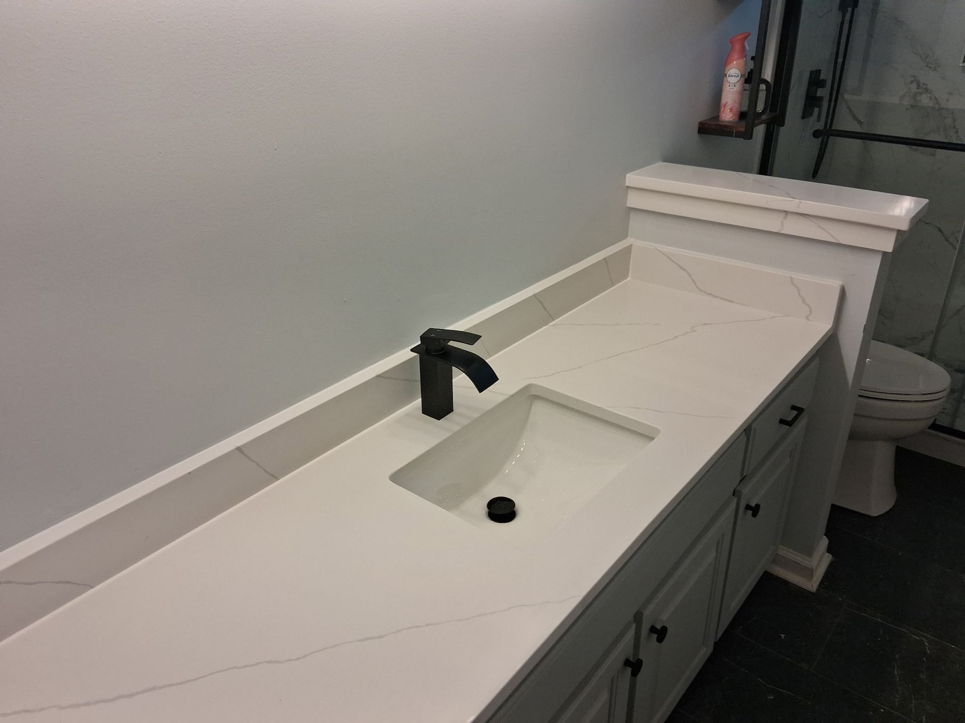 White bathroom vanity with sink, black faucet, and toilet in the background.