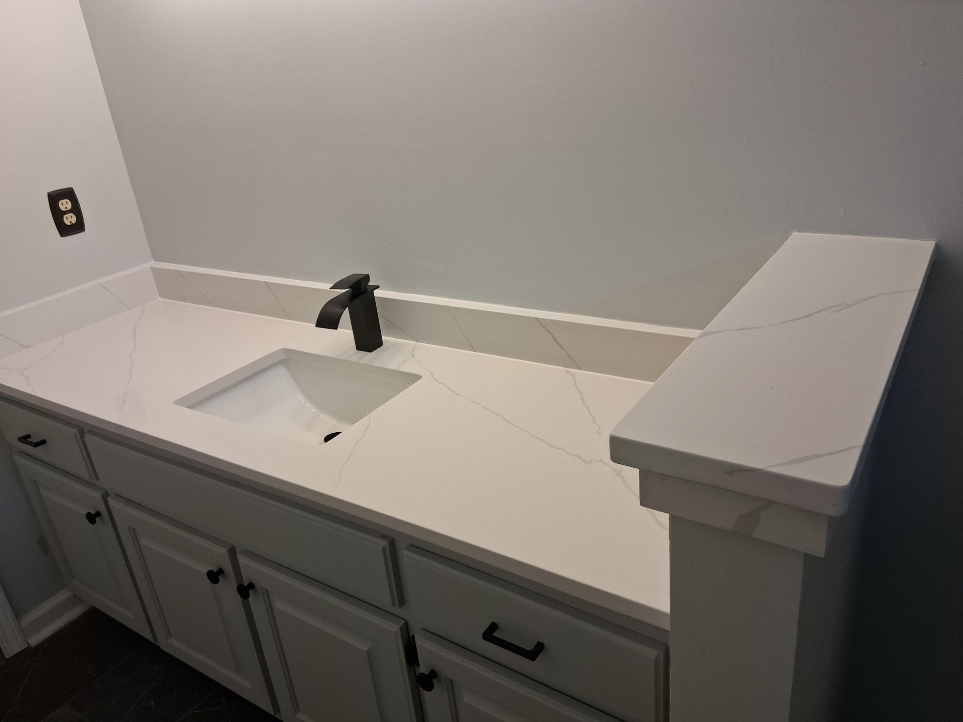 White bathroom vanity with a sink, black faucet, and gray cabinets against a light gray wall.