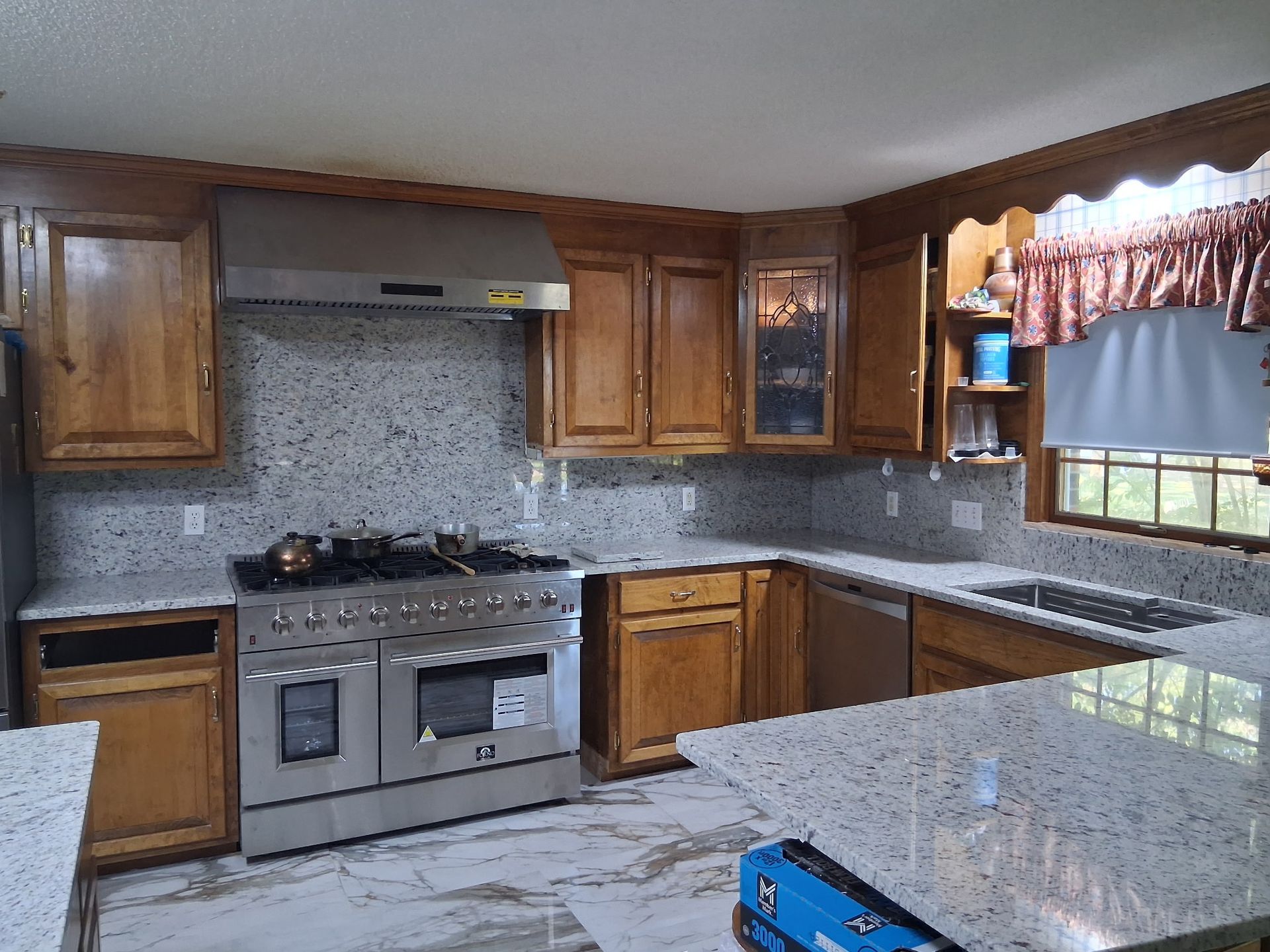 Modern kitchen with wood cabinets, stainless stove, speckled granite counters, and a window over the sink.