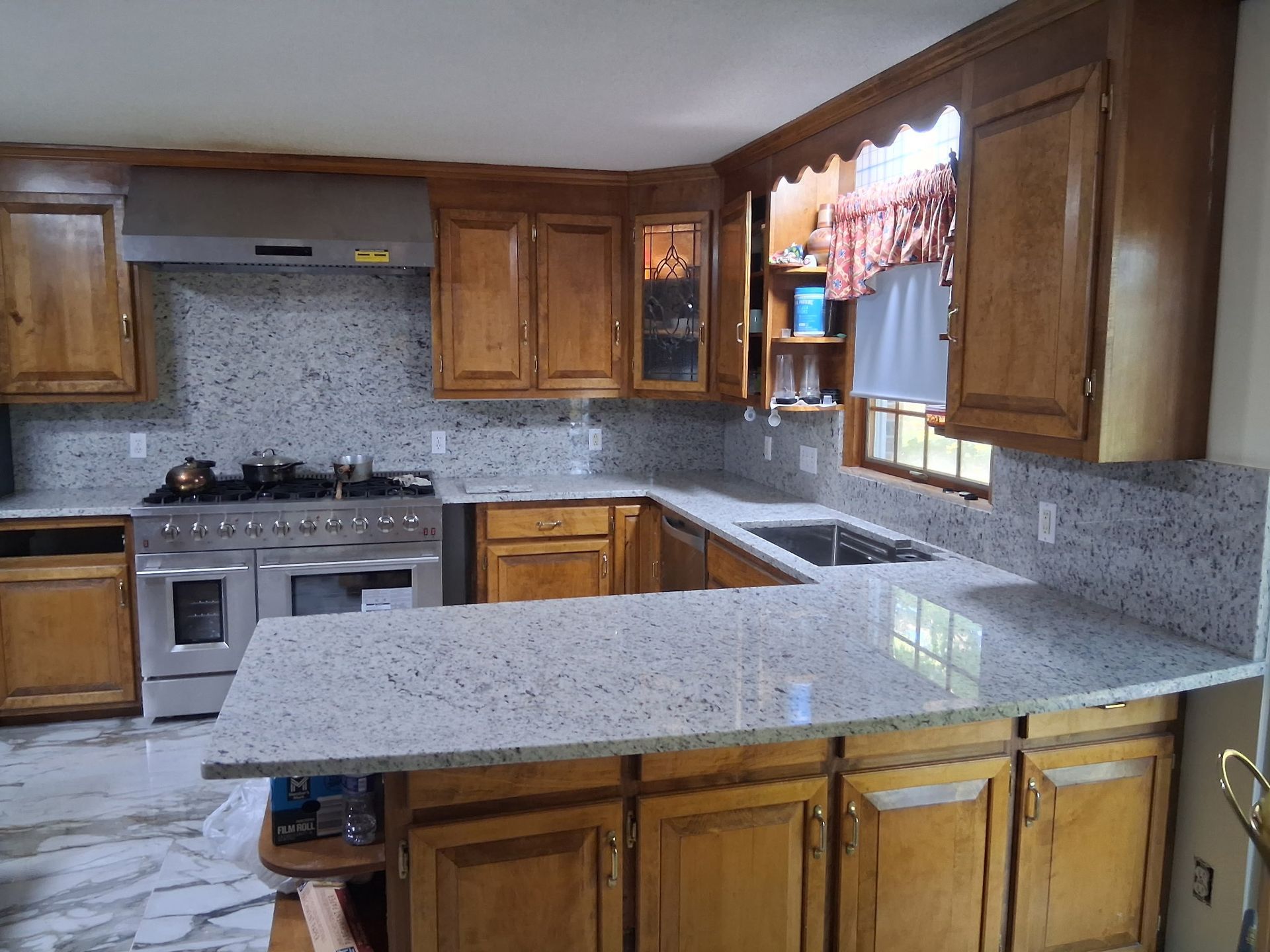 Spacious kitchen with wood cabinets, speckled countertops, and a central island beneath a window.
