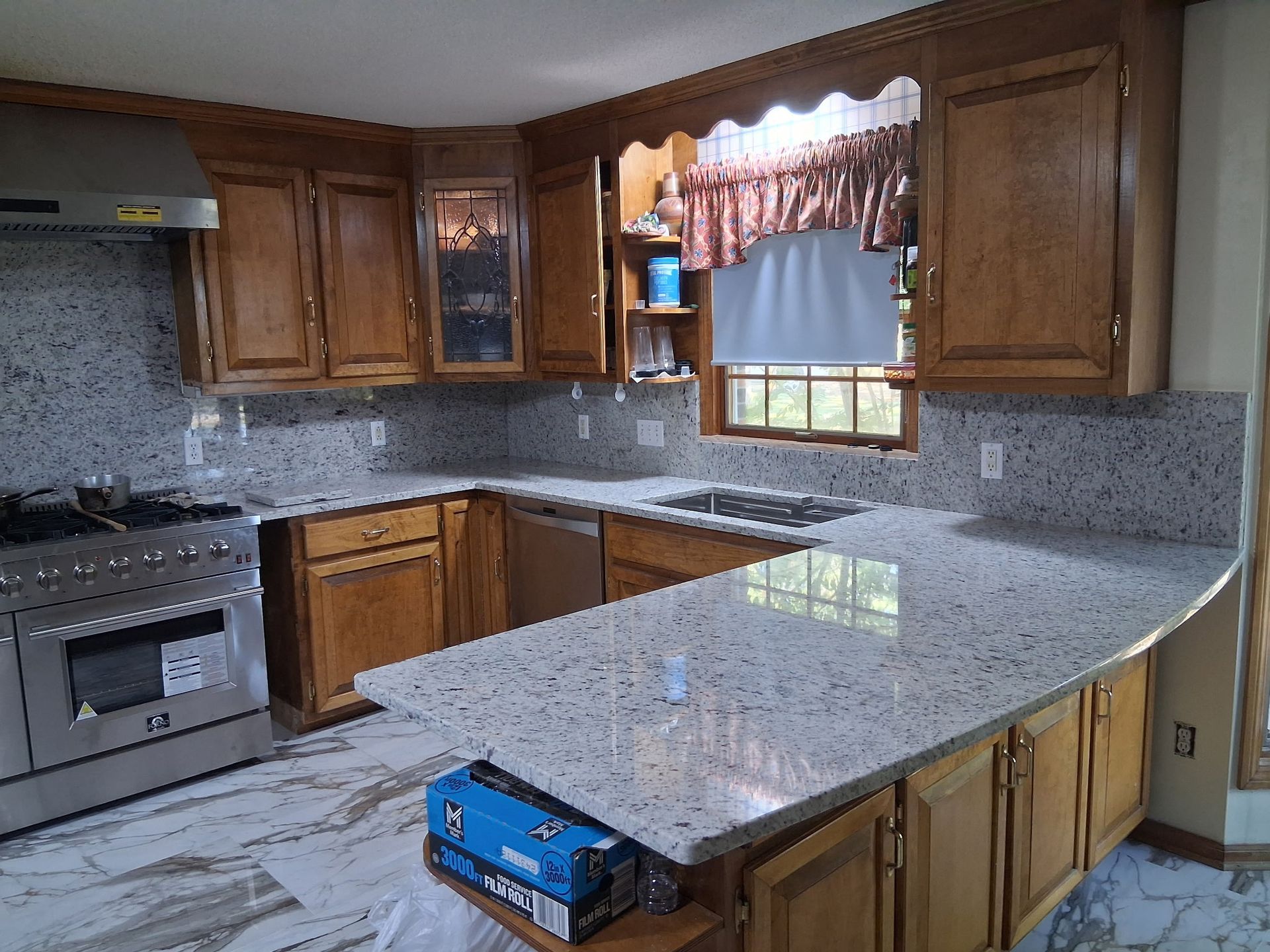 Empty kitchen with wood cabinets, granite counters, stainless stove, and a window over the sink.