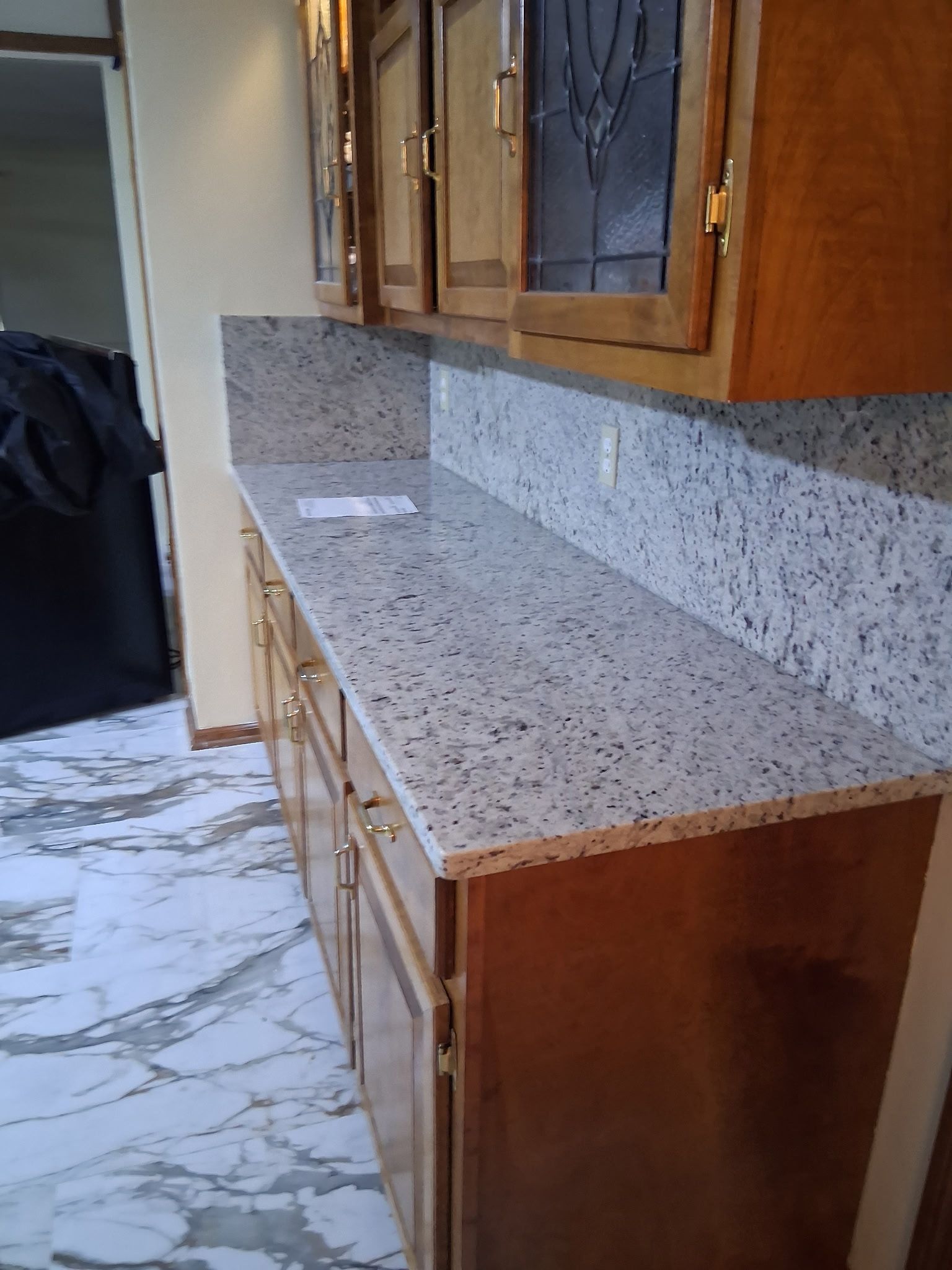 Long granite countertop with wood cabinets and speckled backsplash in a kitchen area