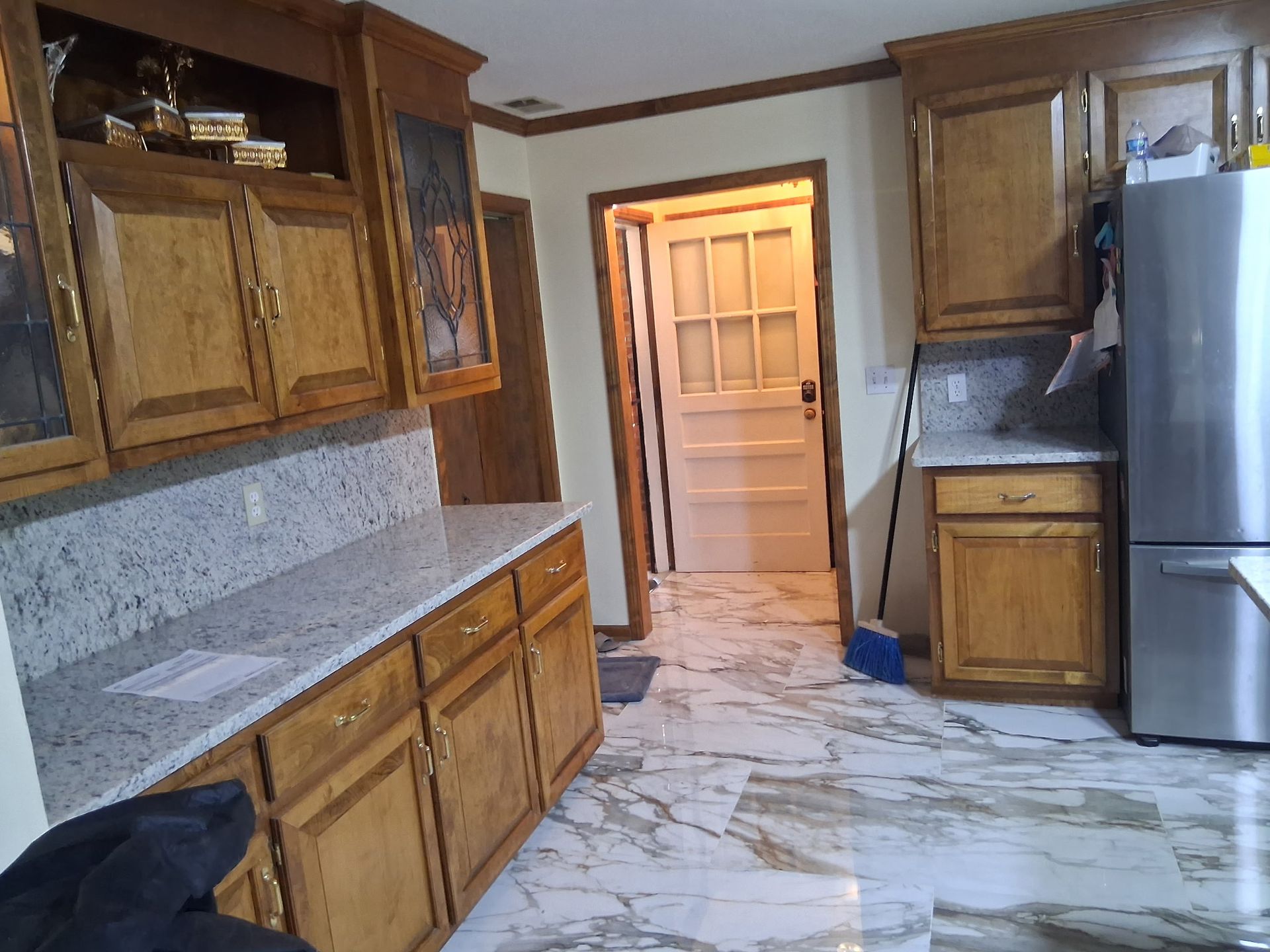 Wood-paneled kitchen with granite counters, marble floor, stainless refrigerator, and open doorway