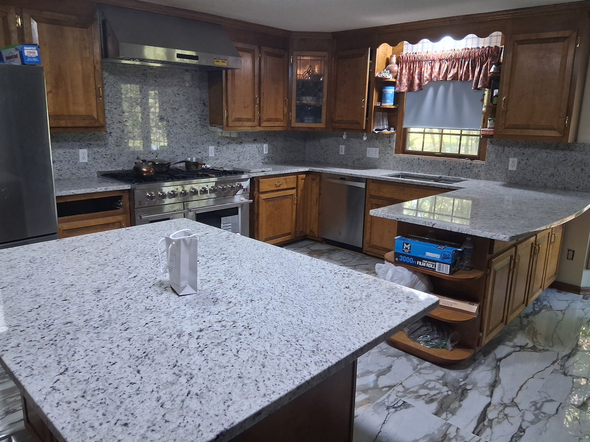 Modern kitchen with brown cabinets, speckled island, granite countertops, and marble-look tile floor
