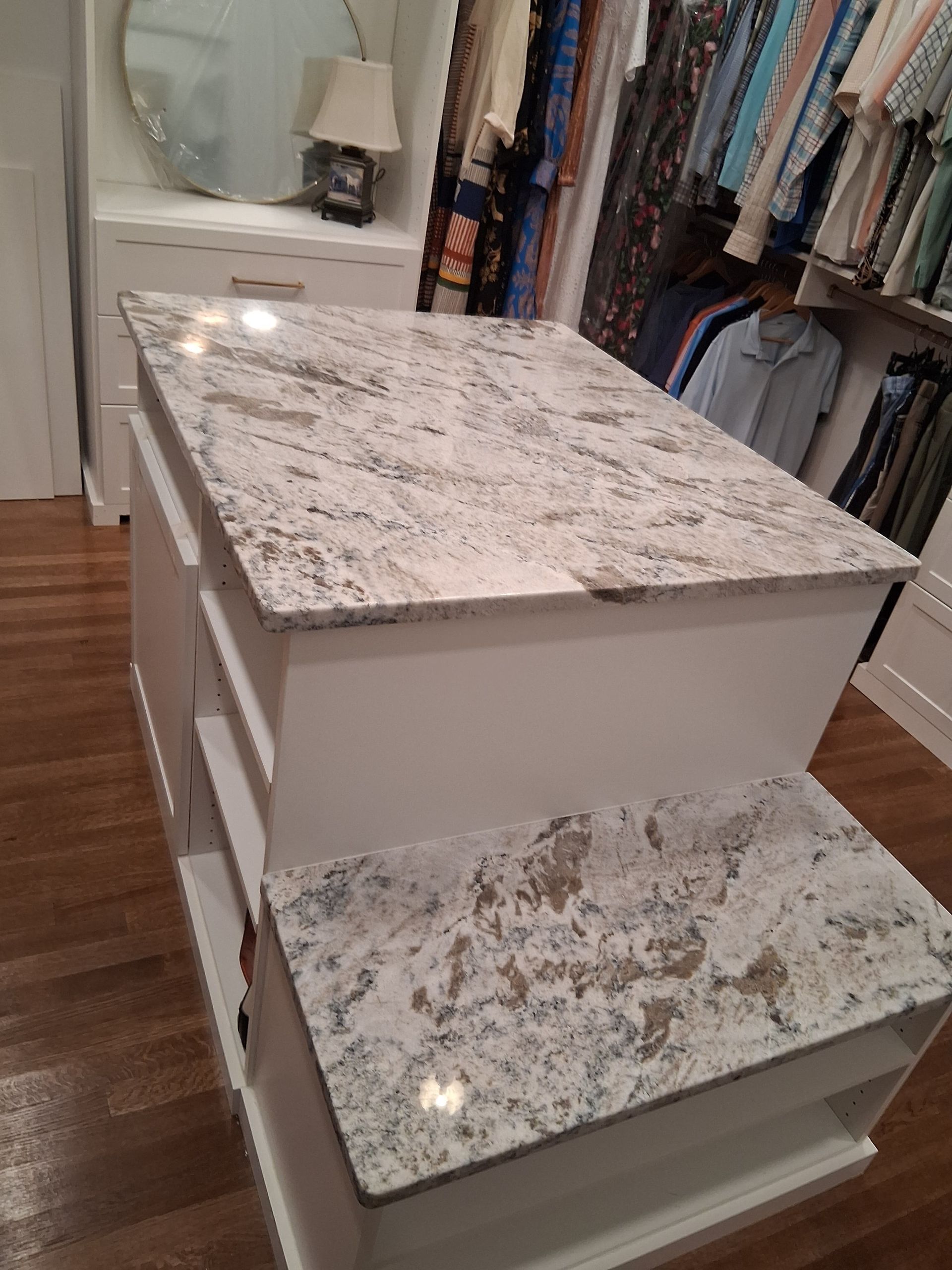 White marble-top dresser in a closet, with drawers open and folded clothes hanging nearby