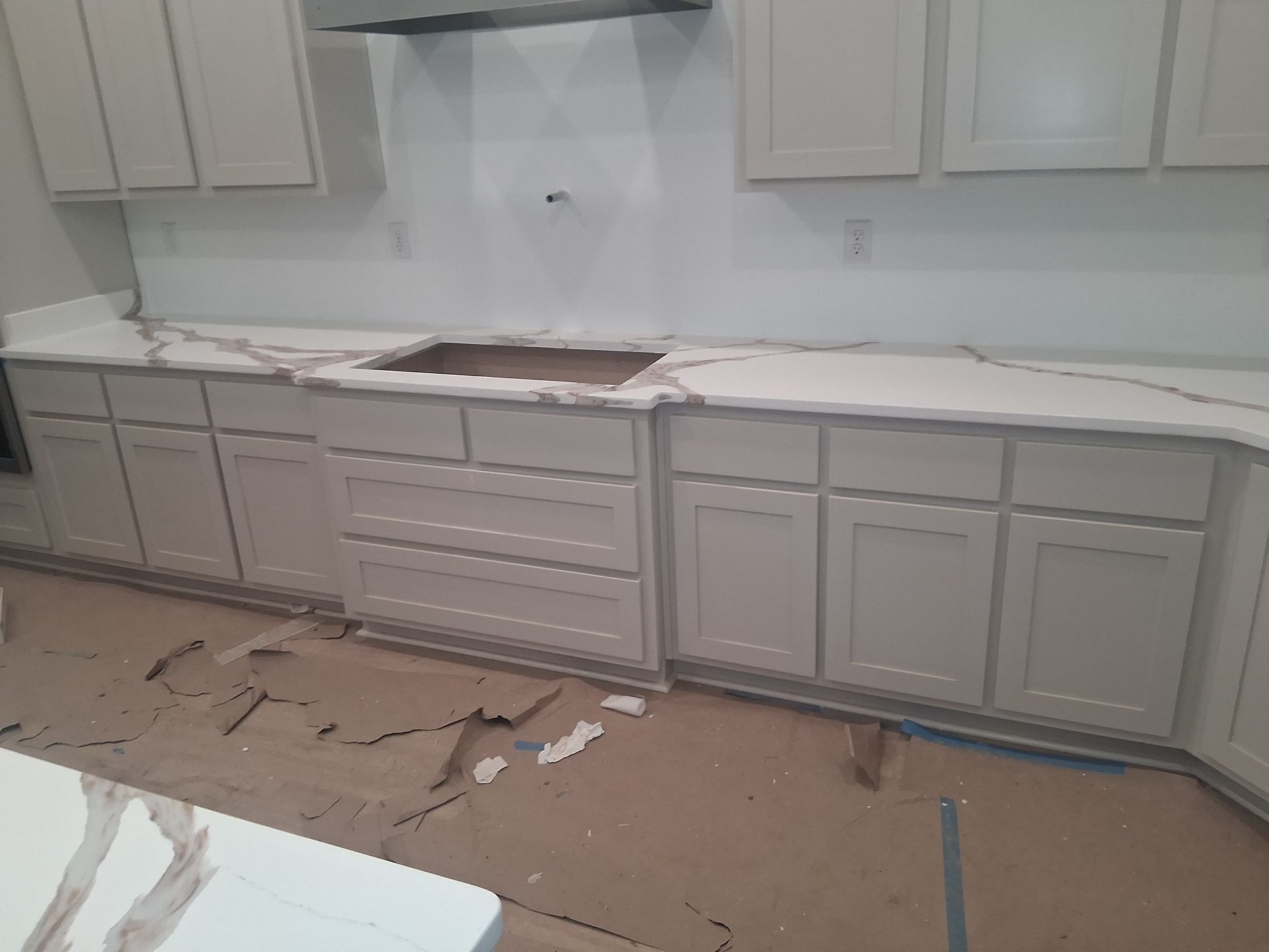 Partially installed white kitchen cabinets and countertop with construction debris on the floor