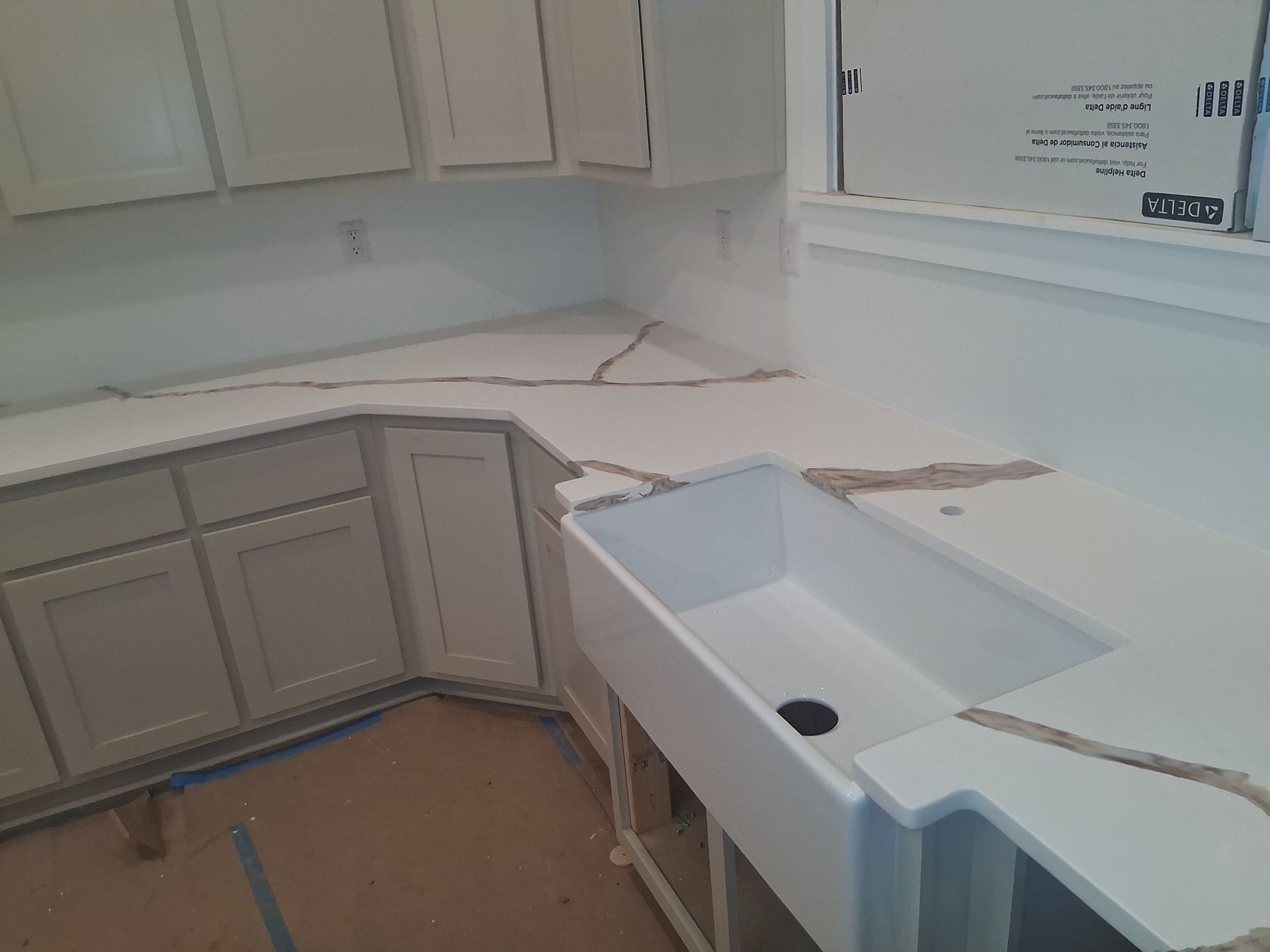 Kitchen with white cabinets and a farmhouse sink under construction, countertops unfinished and debris visible.