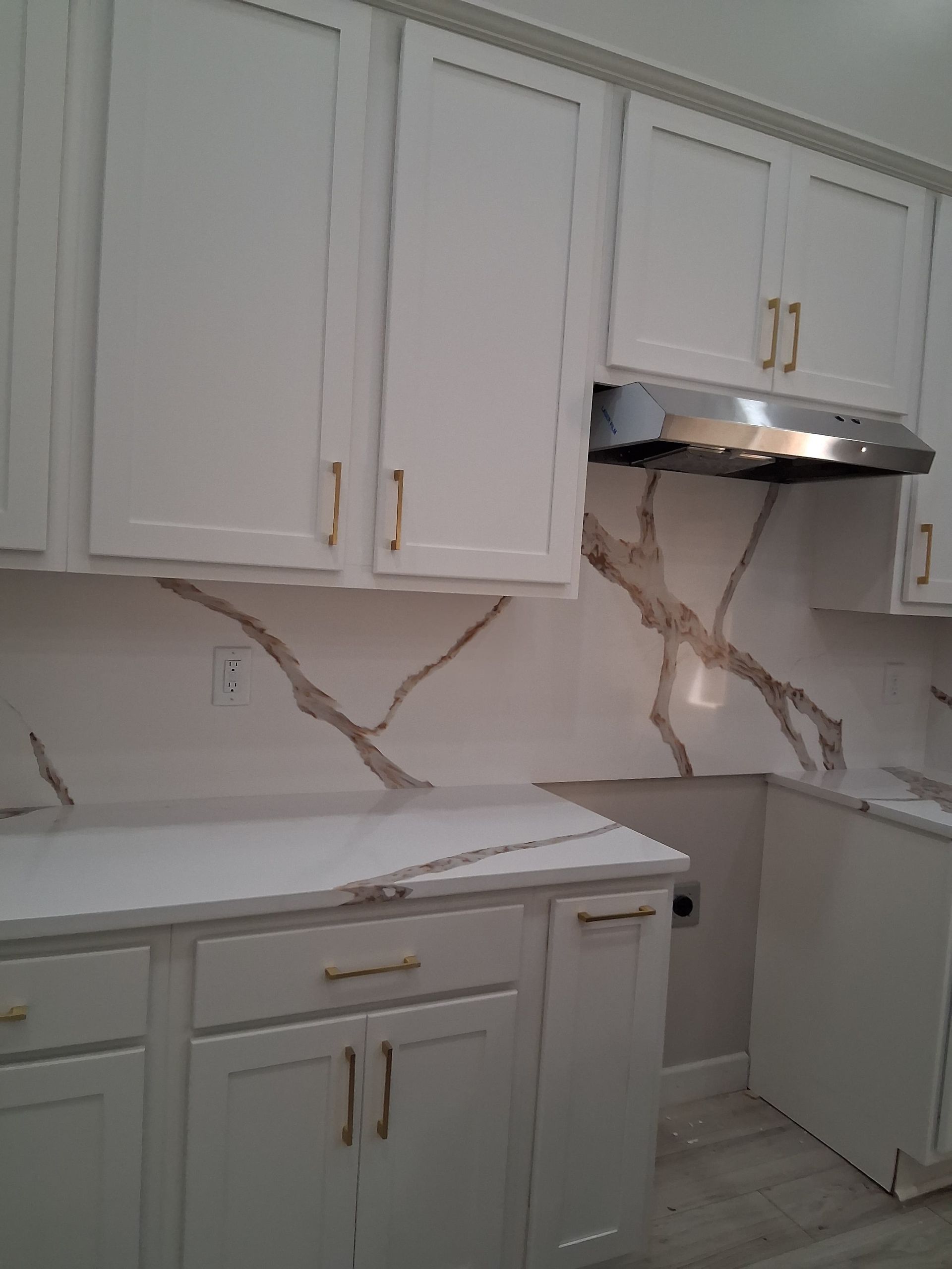 White kitchen with marble countertops, gold handles, and a range hood under installation or repair