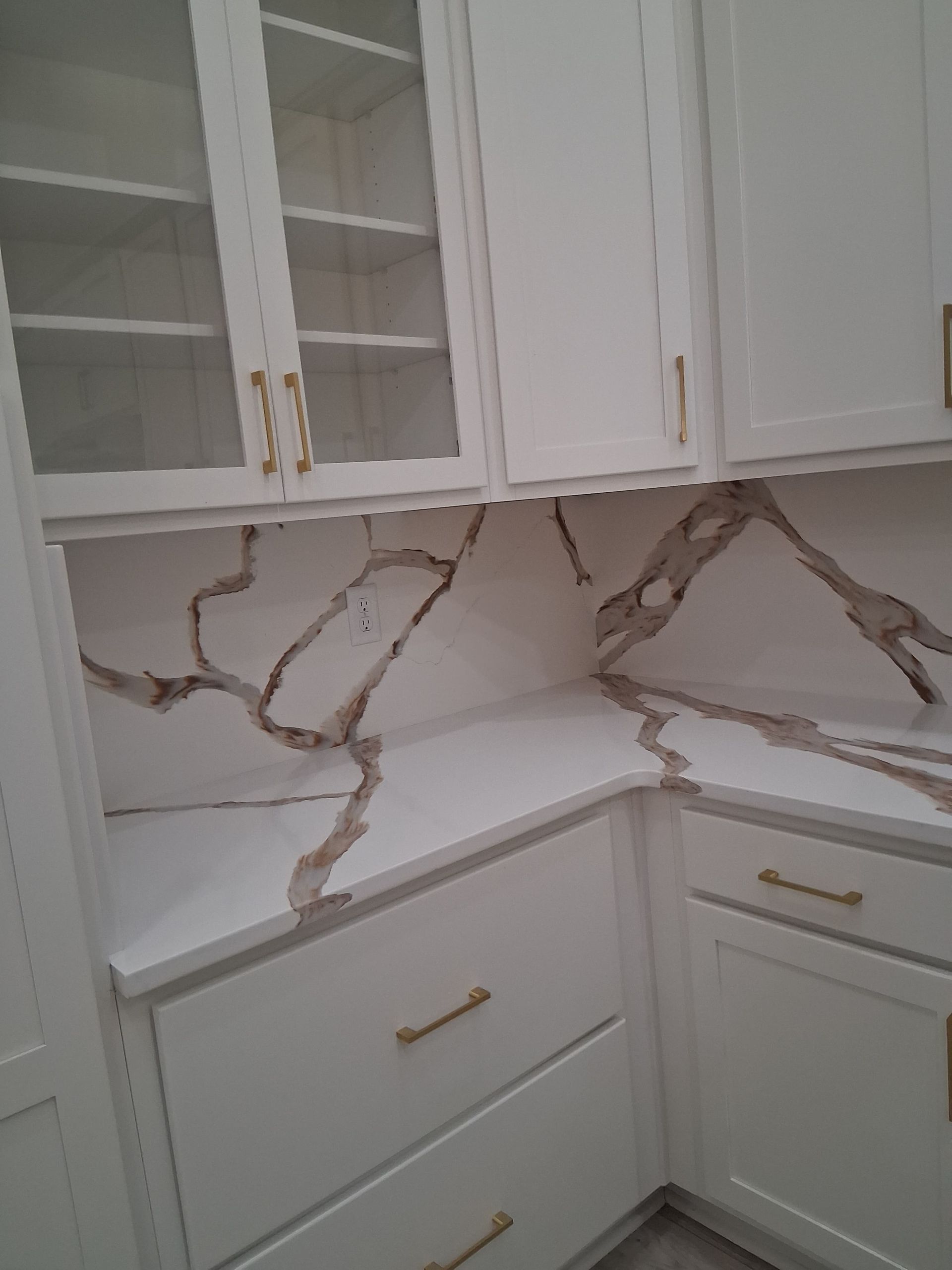 White kitchen cabinets with gold handles and a marble-pattern backsplash and countertop corner