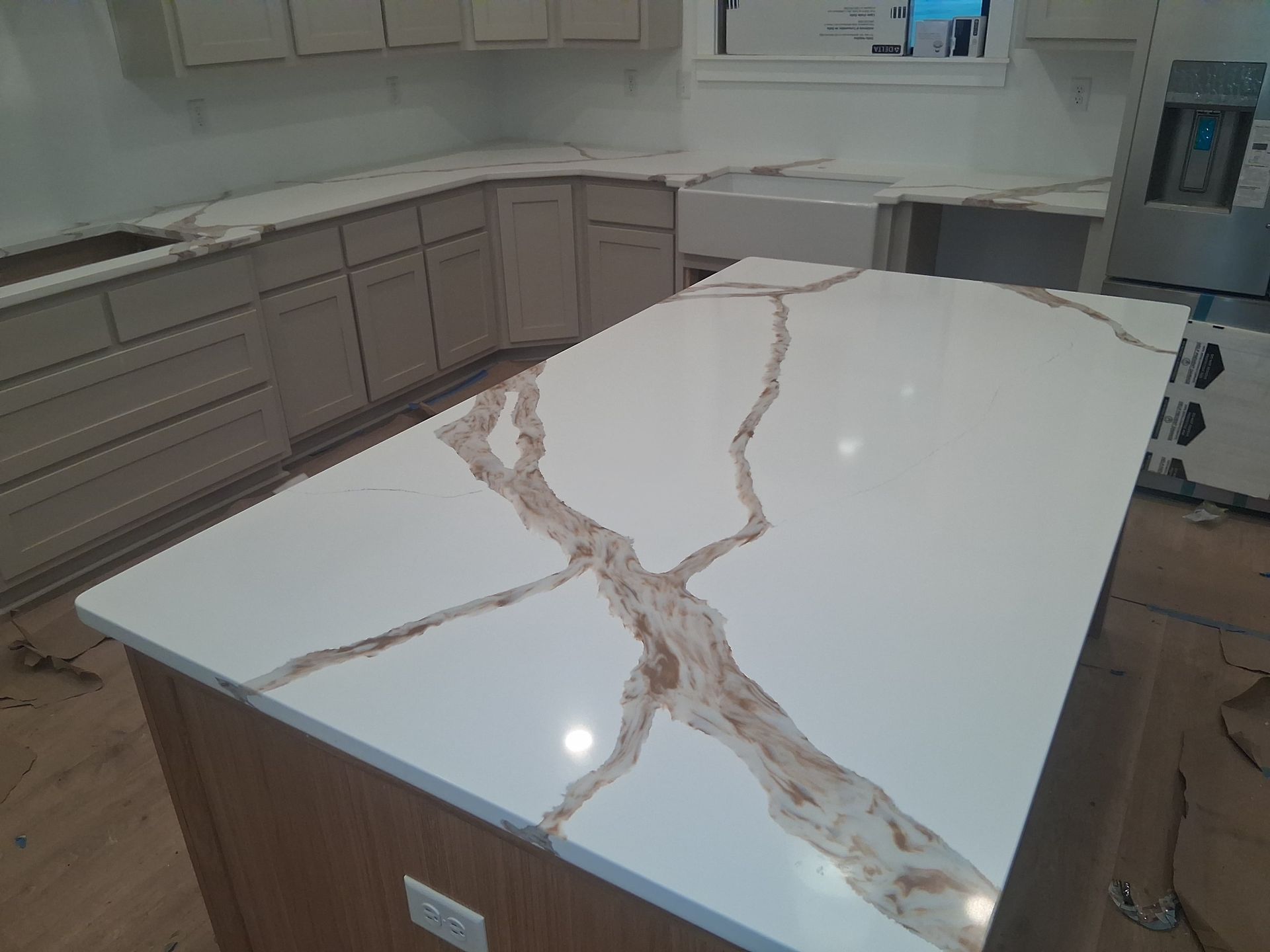 Modern kitchen island with white countertop and pink-gray veining, surrounded by light wood cabinets.
