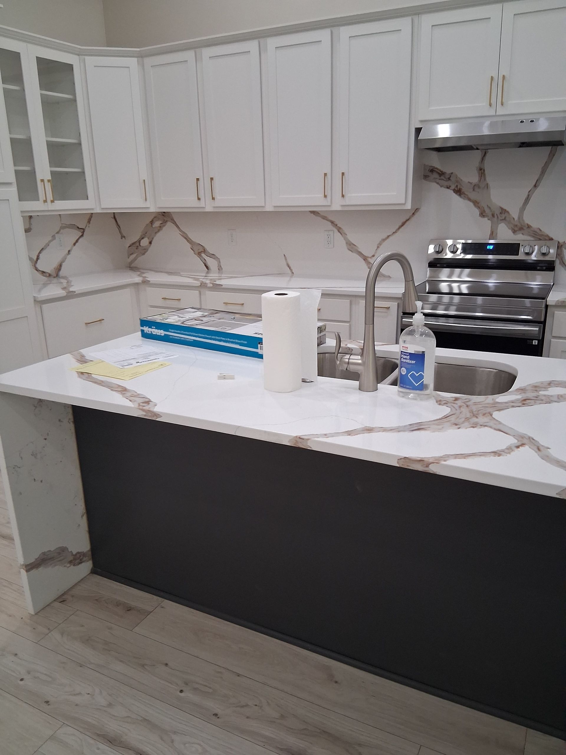 Modern kitchen with white cabinets, marble island, stainless appliances, and a paper towel roll on the counter