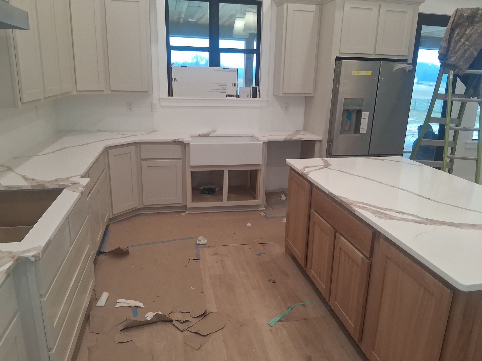 Unfinished kitchen with white cabinets, marble-look island, and debris on the floor near a window.