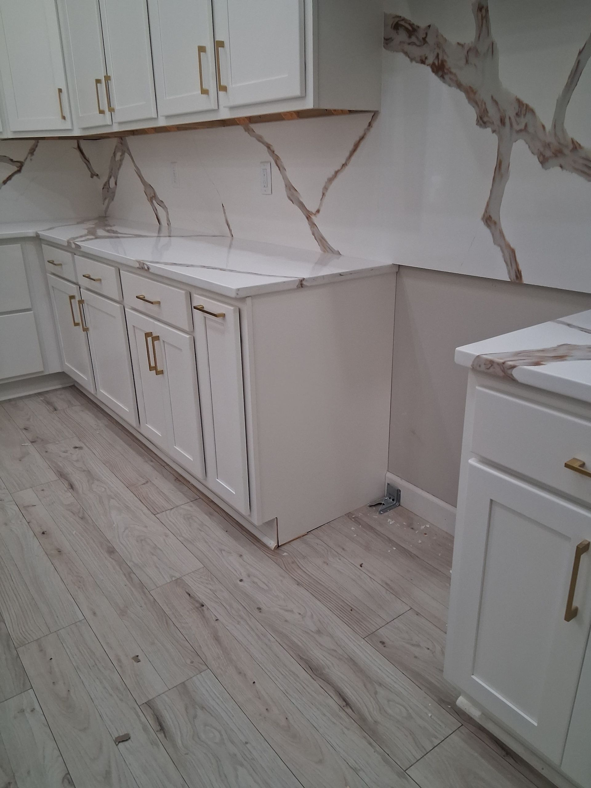 Modern white kitchen with marble-look countertops, gold hardware, and light wood flooring