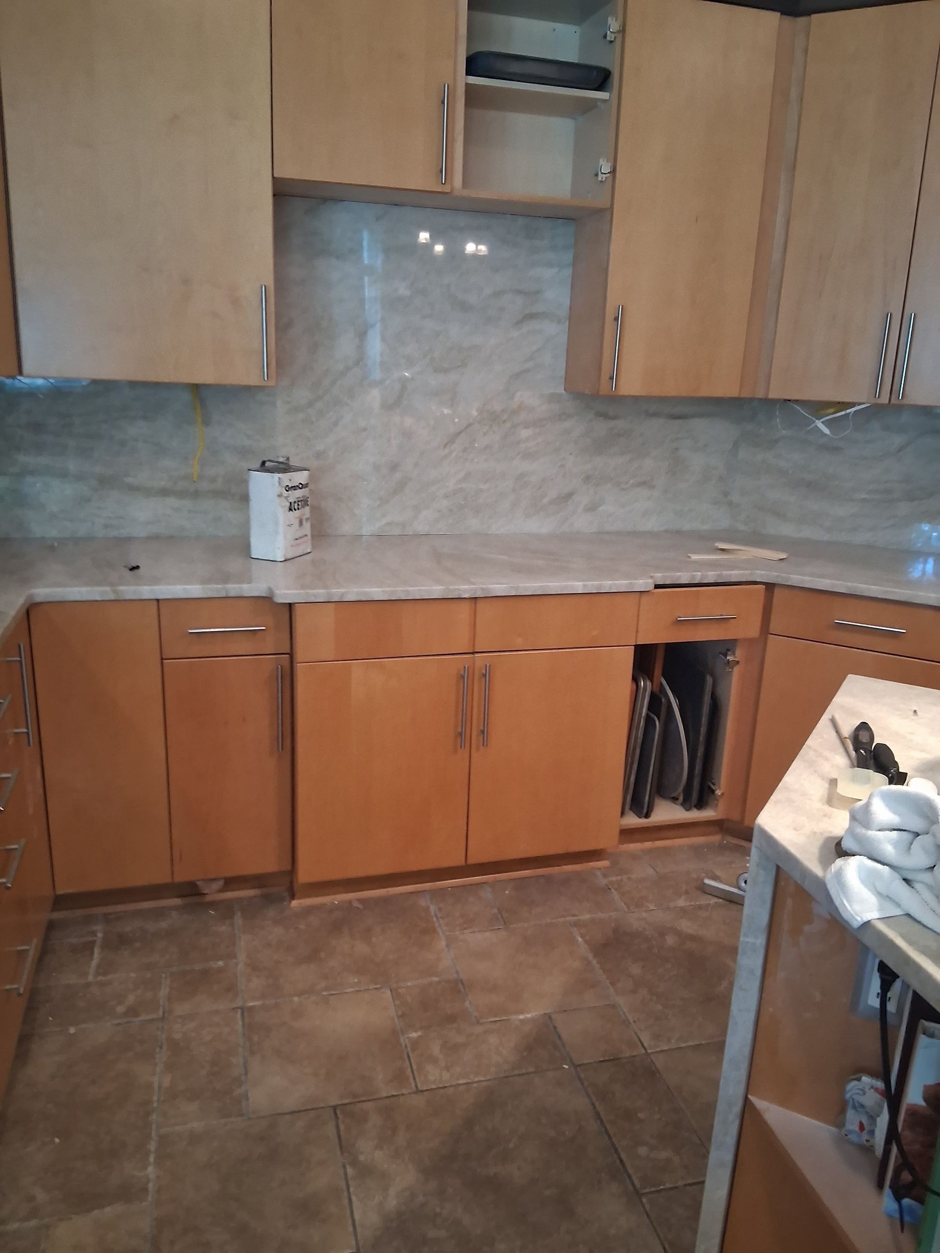 Small kitchen with wooden cabinets, tiled backsplash, countertop, and brown tile floor.